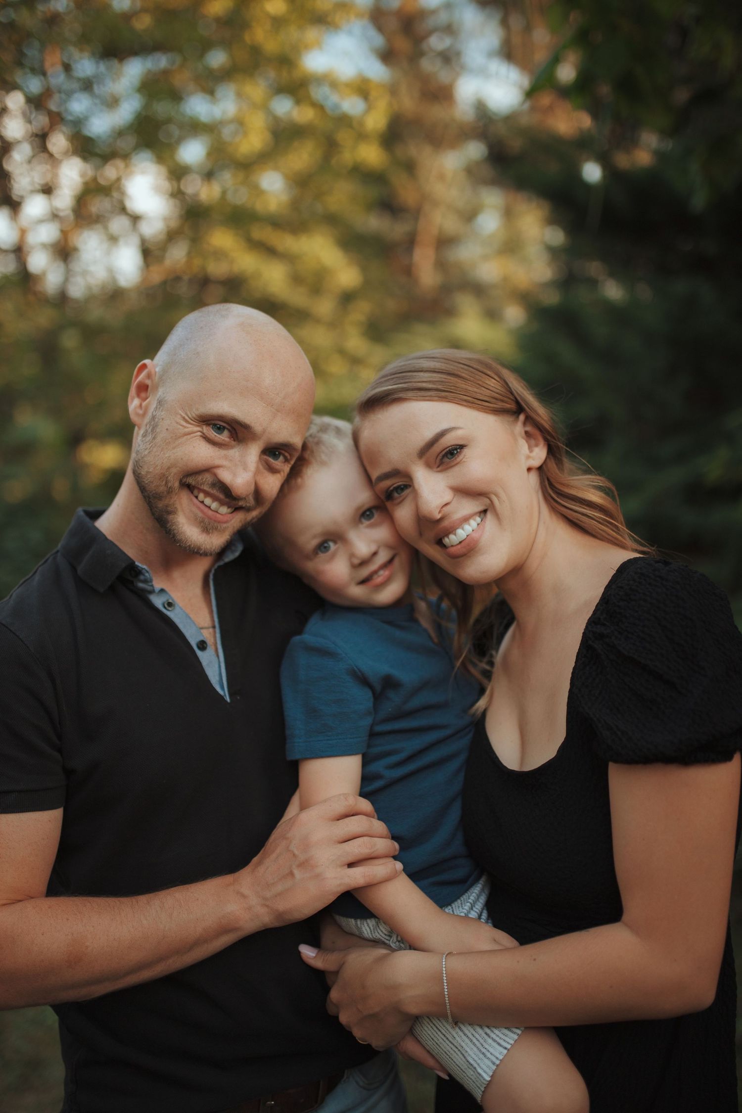 A happy family of three shares a warm embrace during an outdoor sunset photoshoot.