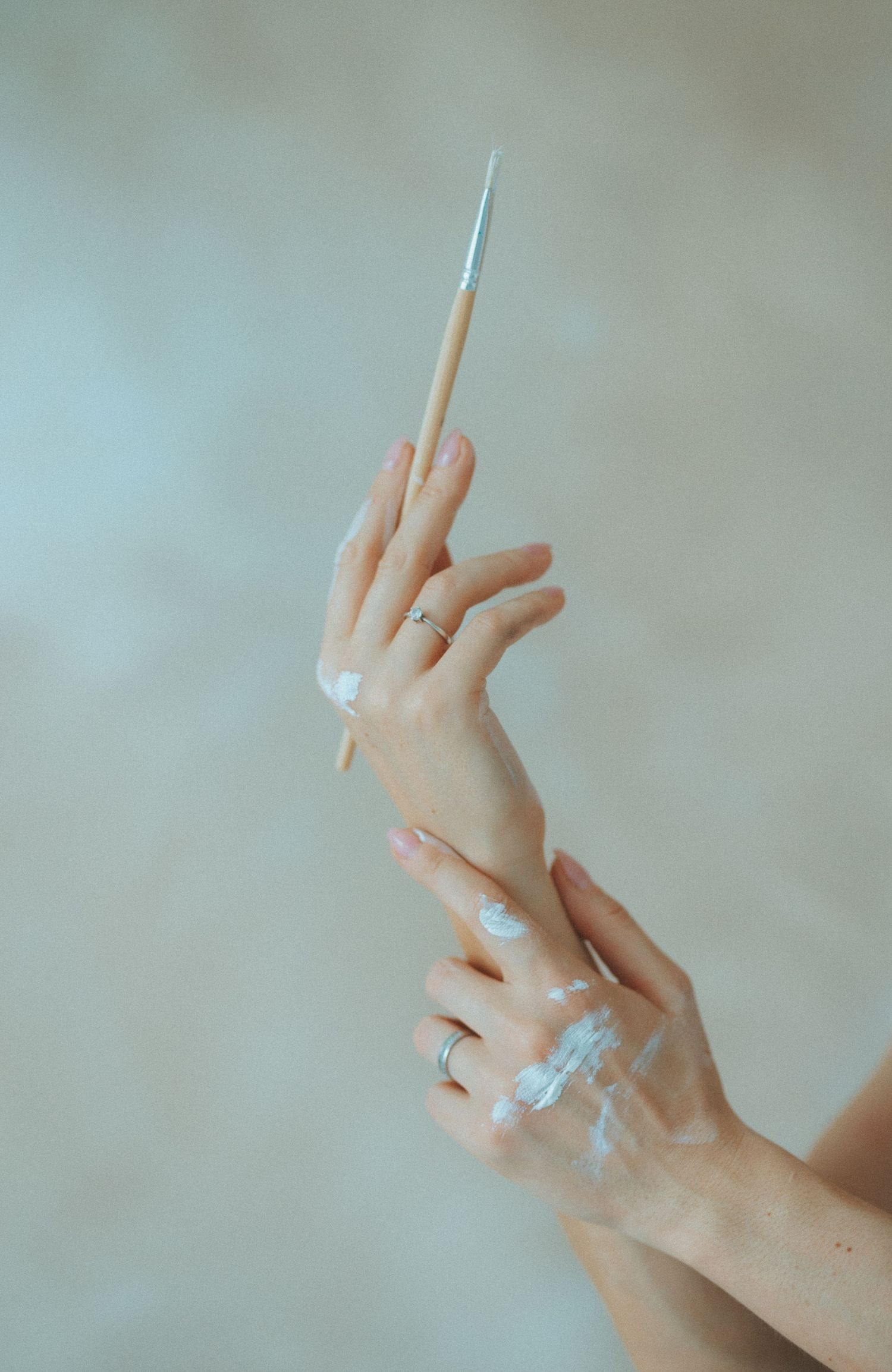 Close-up of hands with rings making artistic gestures against neutral background.