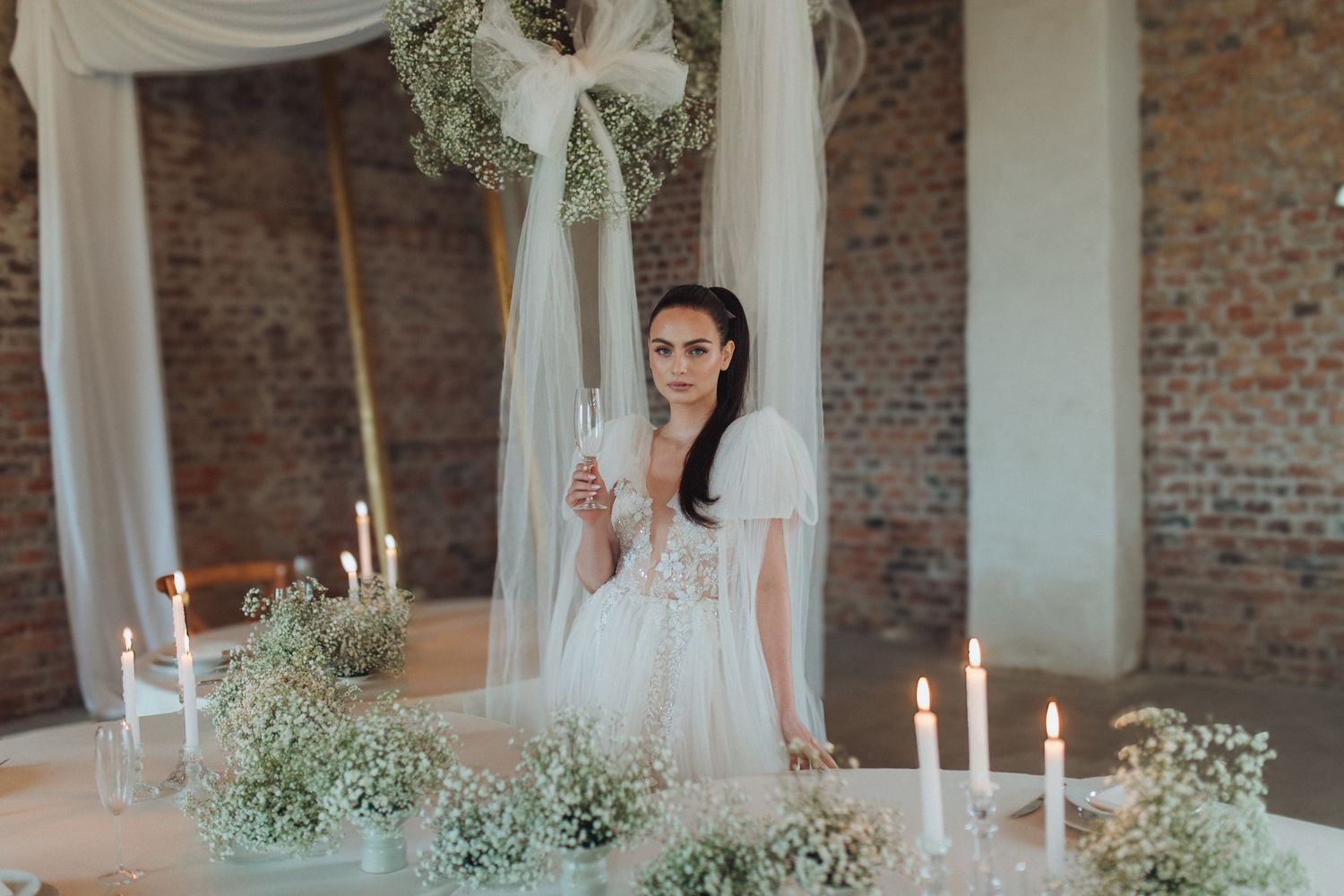 Event space decorated with white fabric draping and floral arrangements against rustic brick walls.