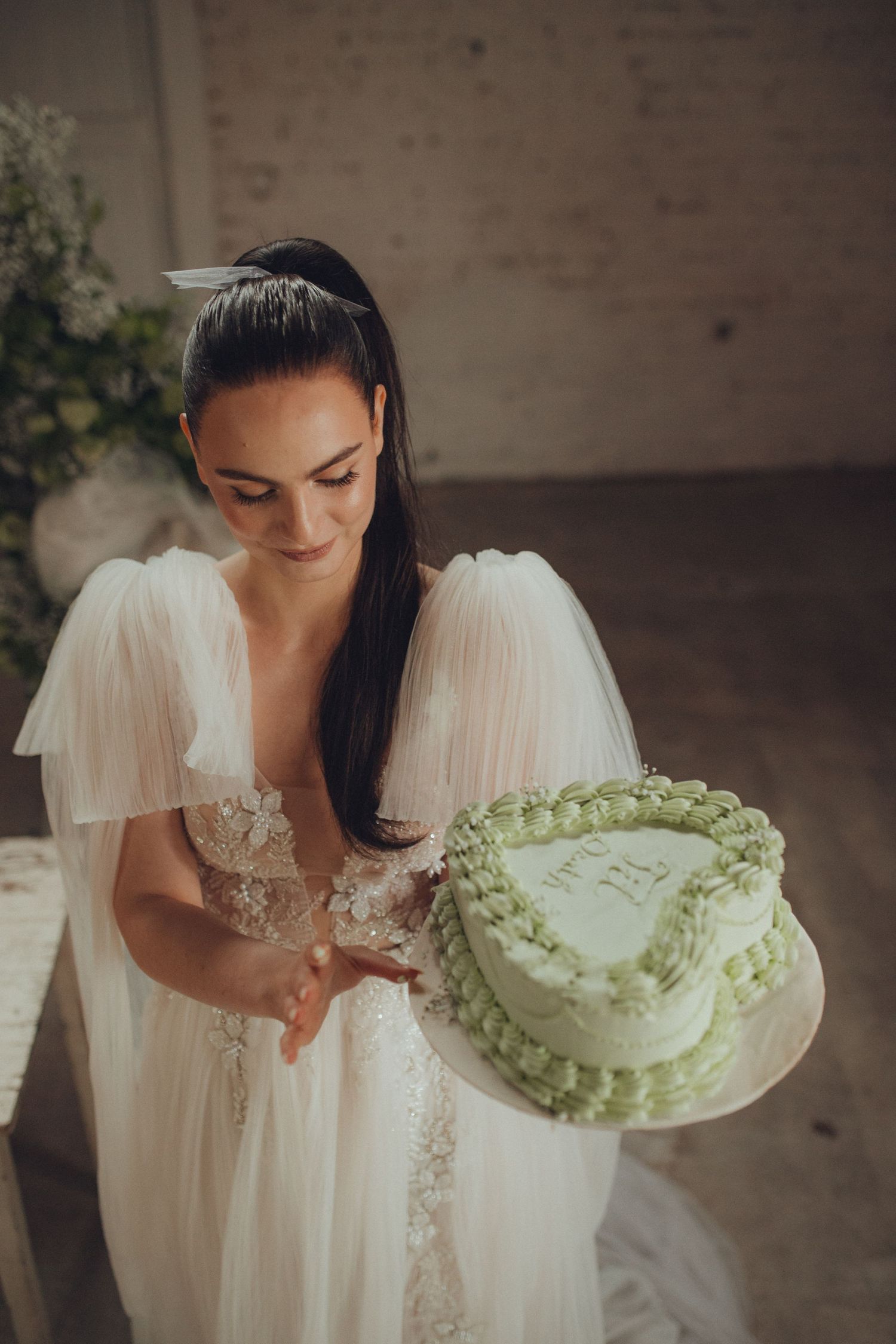 Wedding dress detail shot with decorative green and white cake in rustic setting.