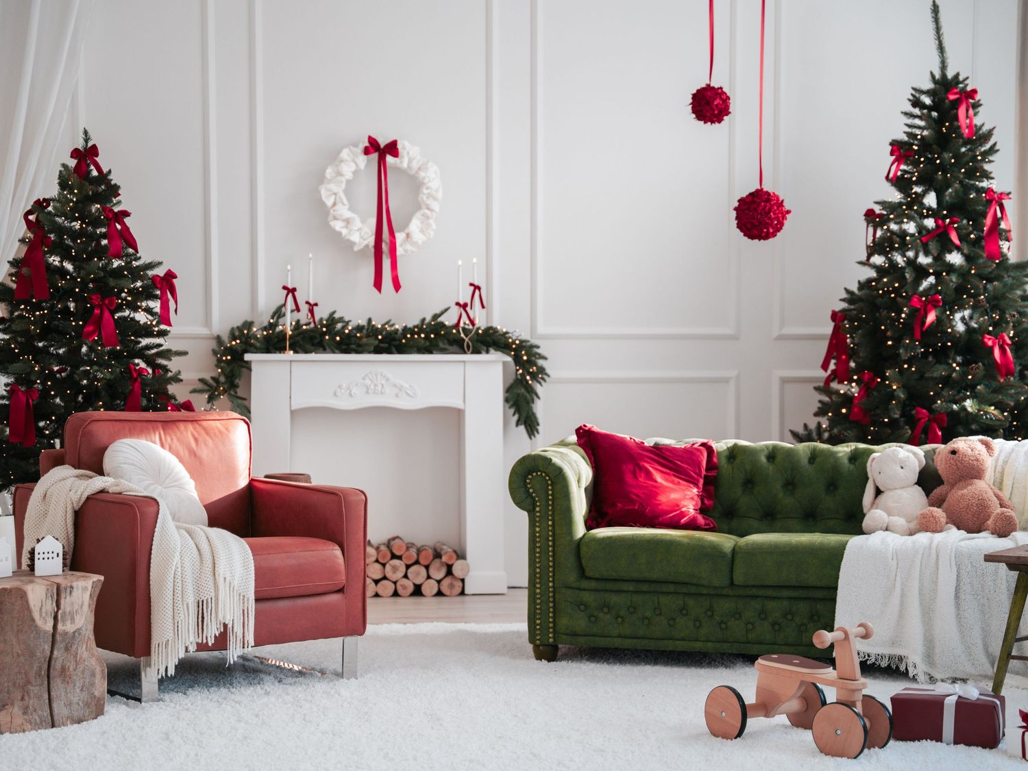 Festive living room with green sofa, red accents, decorated Christmas trees, and a white fireplace mantel.