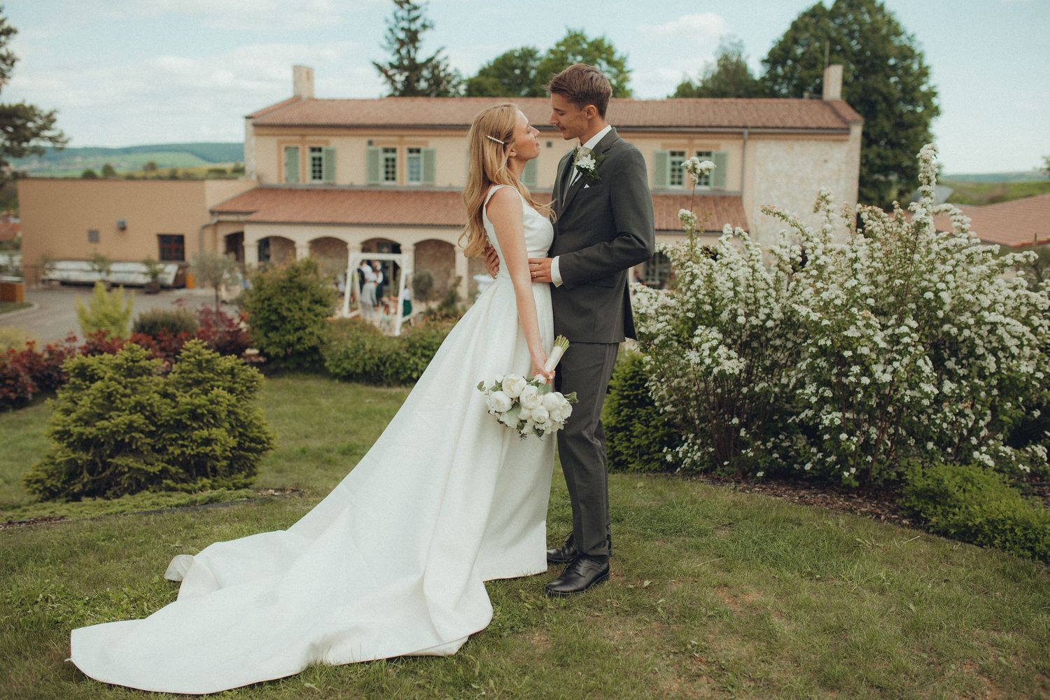 Wedding couple walks through manicured garden with Mediterranean style architecture.