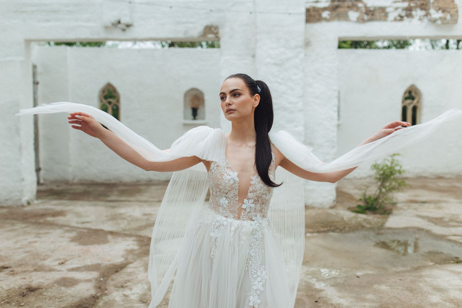 Flowing white wedding gown creates dramatic movement against white architectural backdrop.