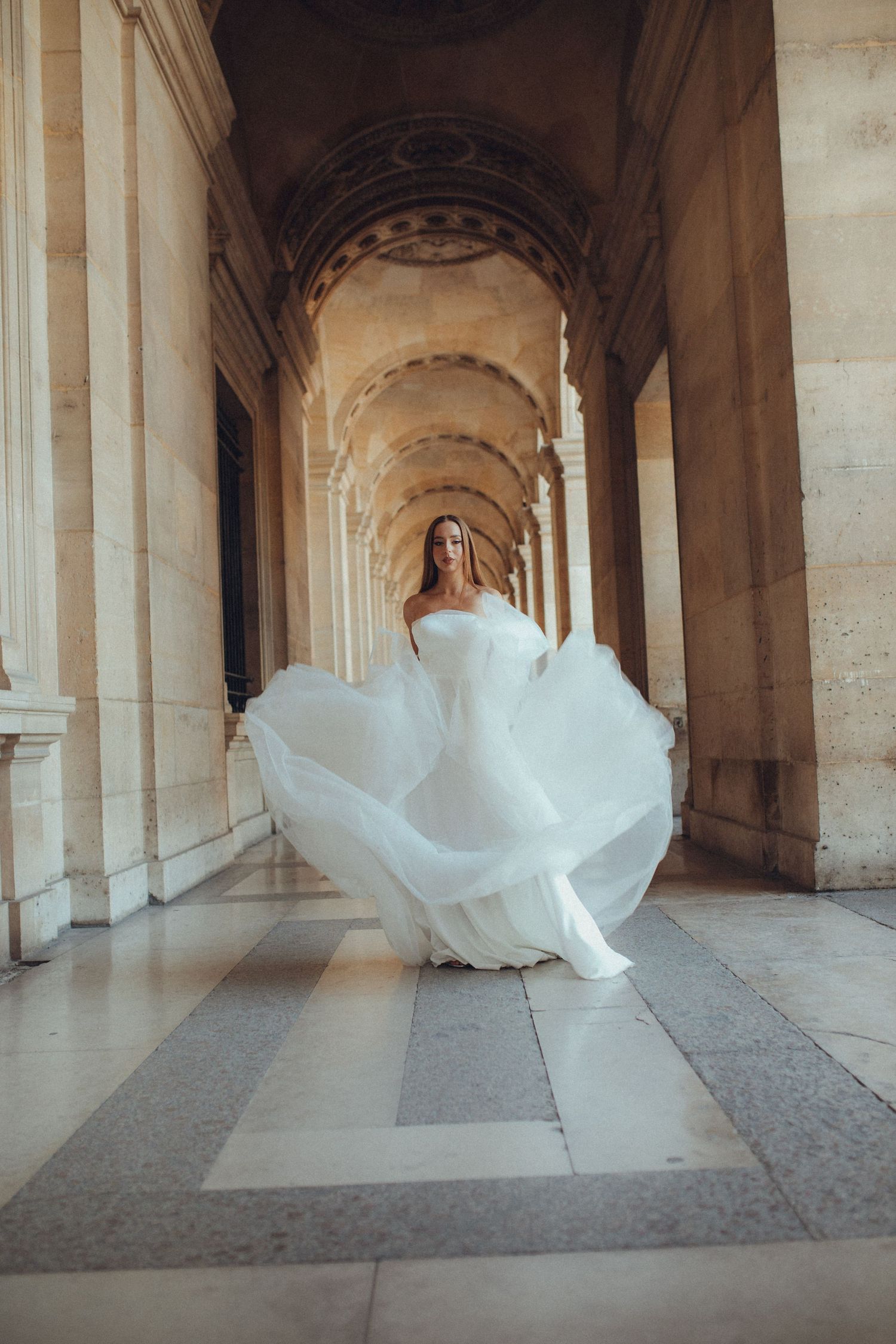White flowing dress captured in motion through a grand colonnade hallway.