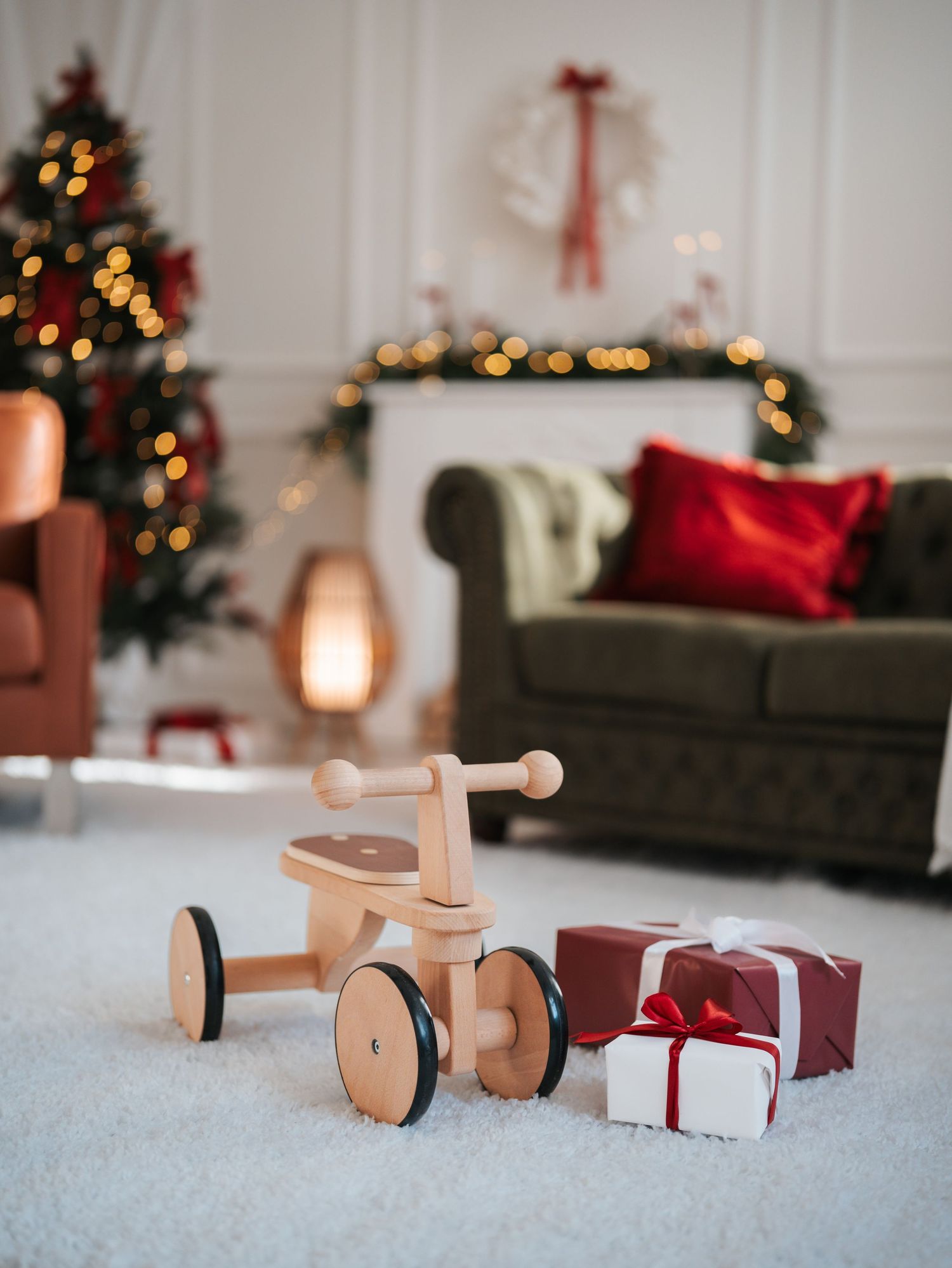 Wooden balance bike toy with Christmas gifts beside it in a festive living room with decorated tree and fireplace.
