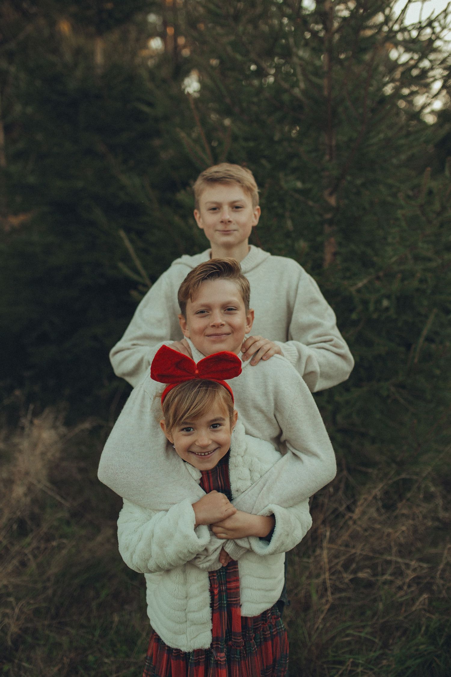 Two children in festive winter outfits pose playfully together against a dark outdoor background.