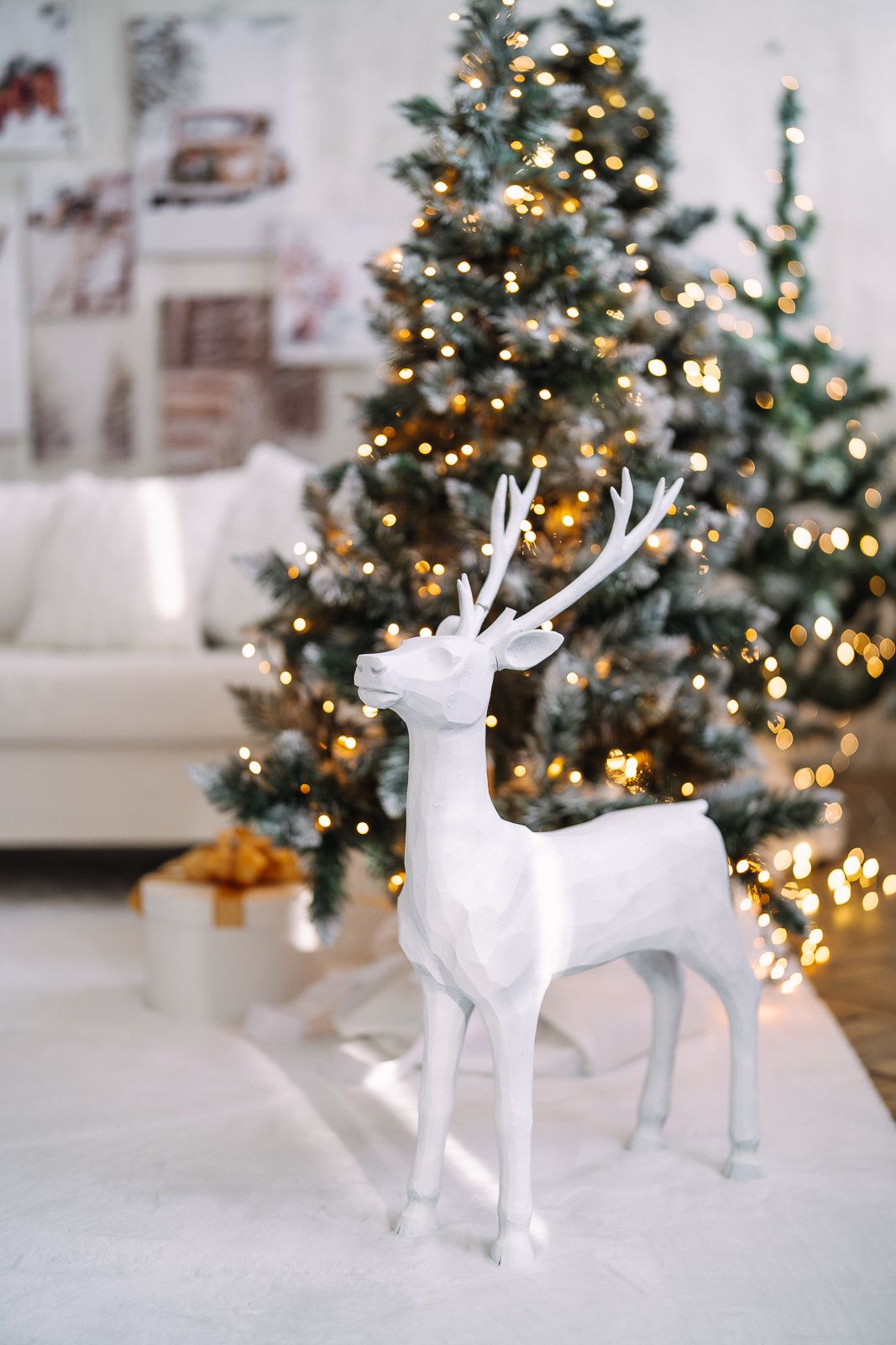 White ceramic reindeer decorations displayed in front of a lit Christmas tree with golden lights and ornaments.