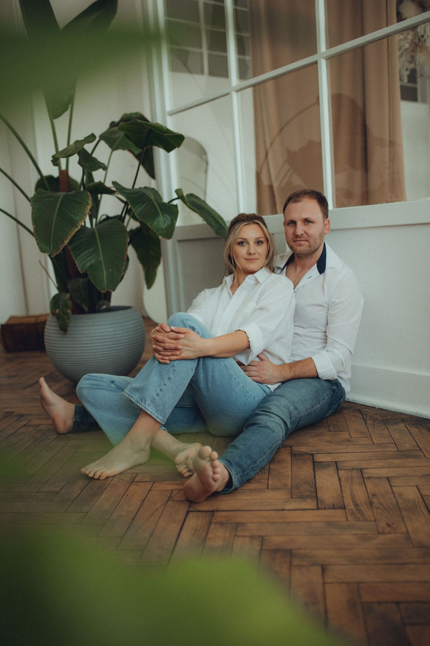 Casual lifestyle portrait of couple relaxing on parquet floor near potted plant.