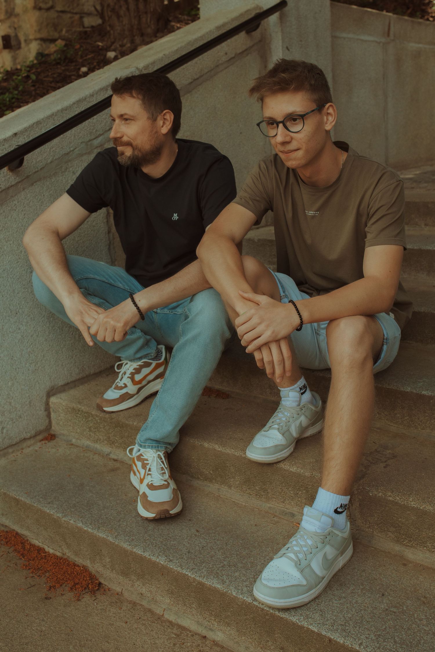 Two people sitting casually on concrete steps wearing t-shirts and sneakers.