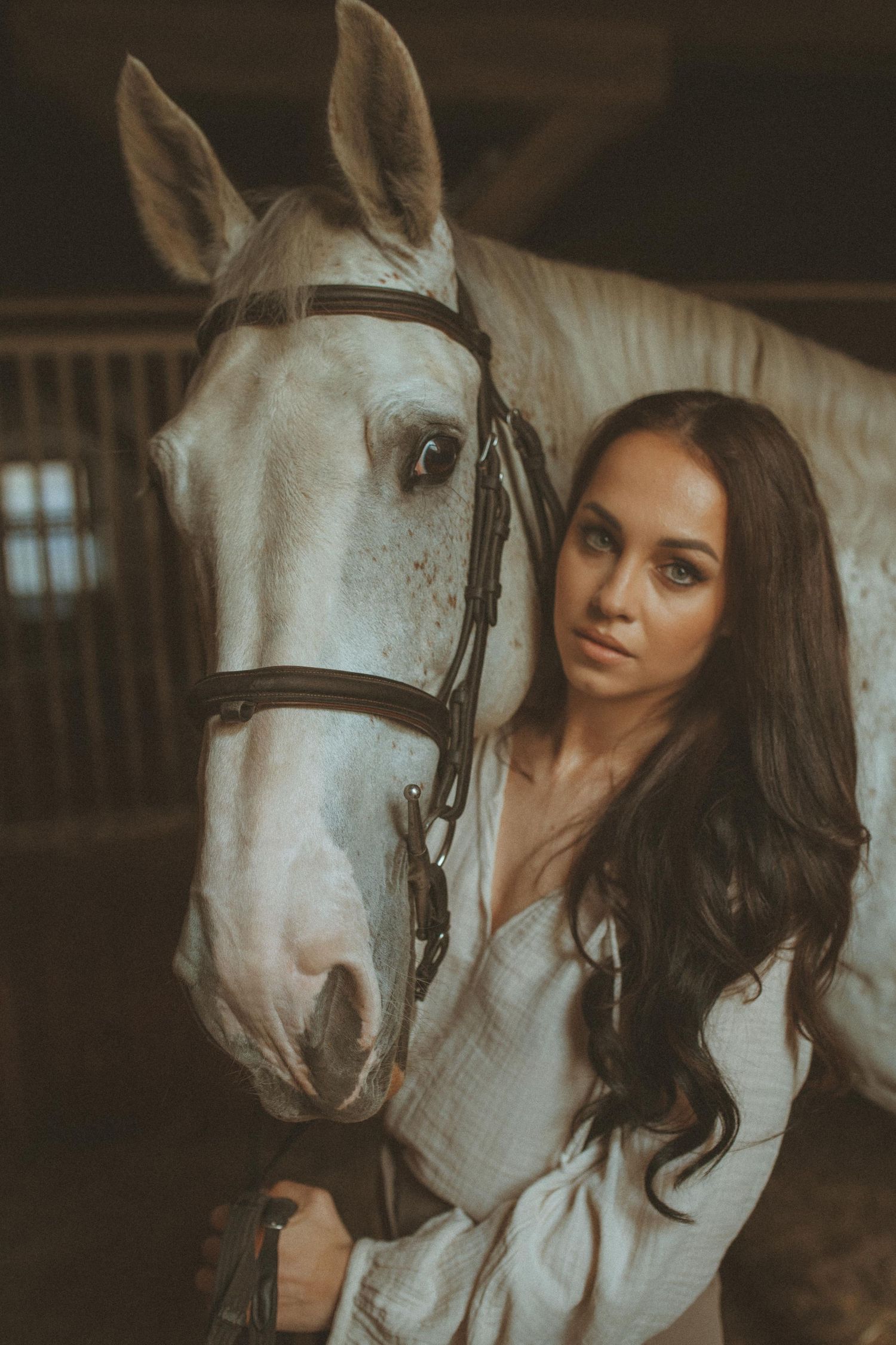 Moody portrait with a white horse in a rustic stable setting.
