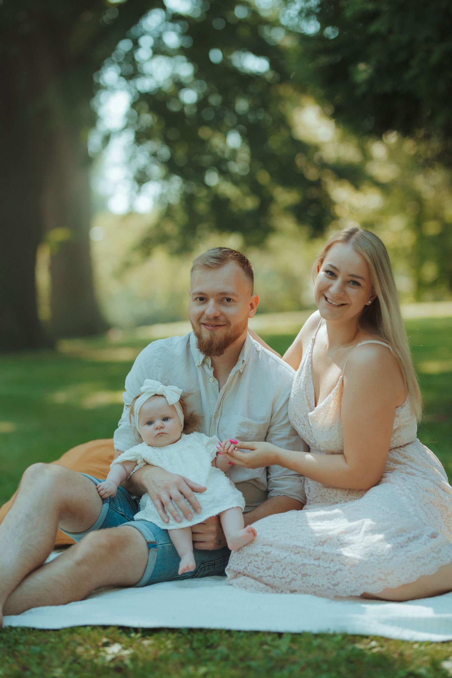Family sitting together on white blanket during sunny summer day in park.