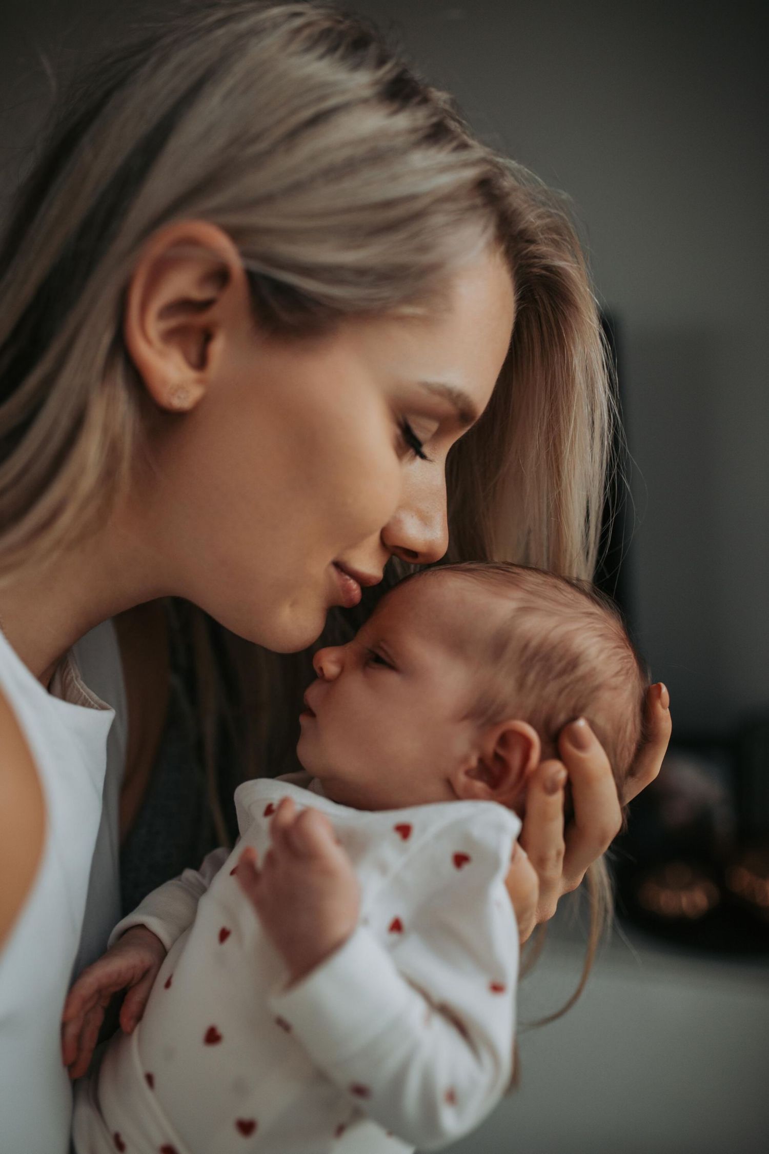 A tender parental moment shows love and bonding with a small newborn baby wearing a white onesie with red hearts.