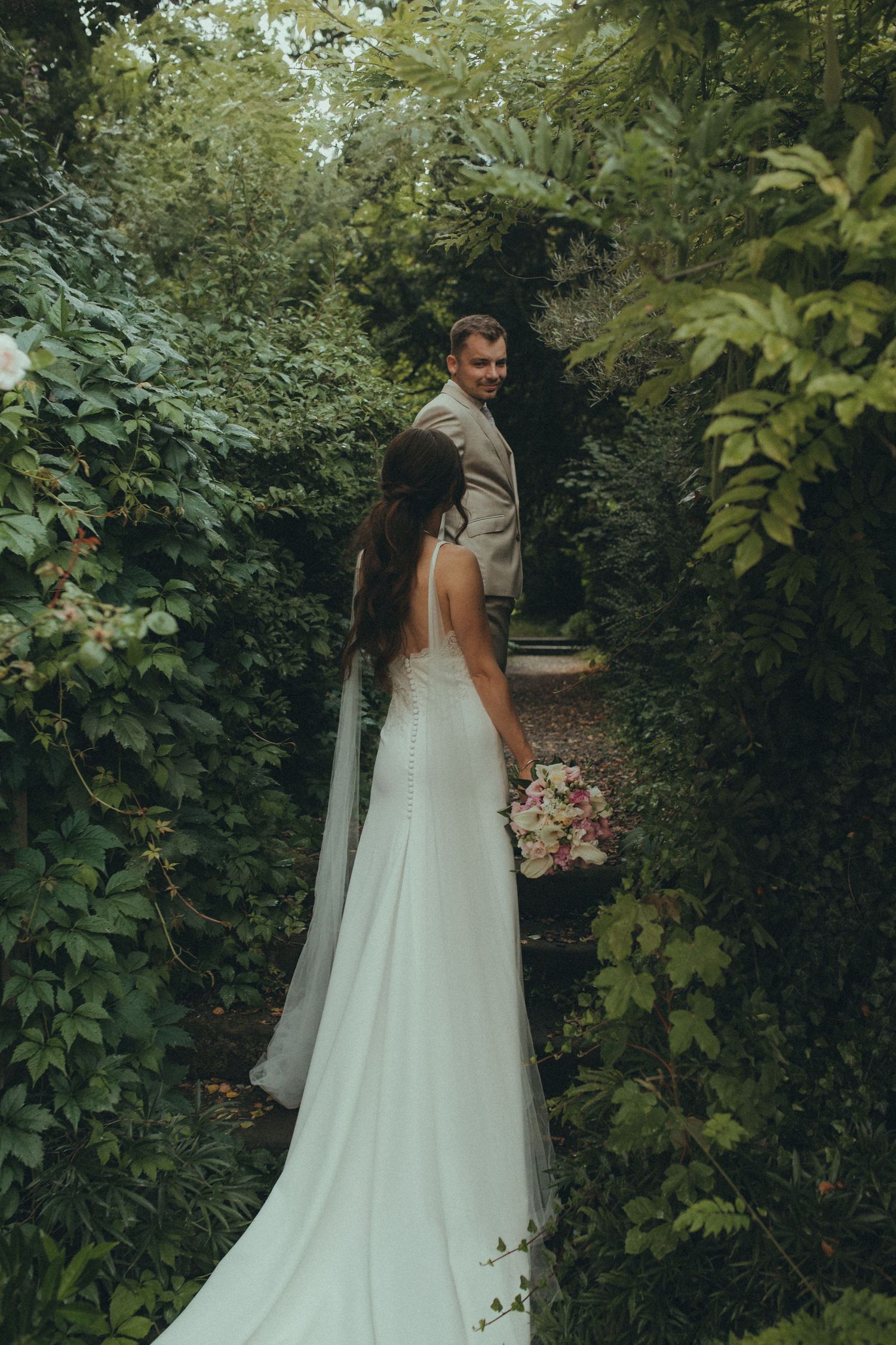 A couple shares a romantic moment in a lush garden setting with trailing greenery and natural light.