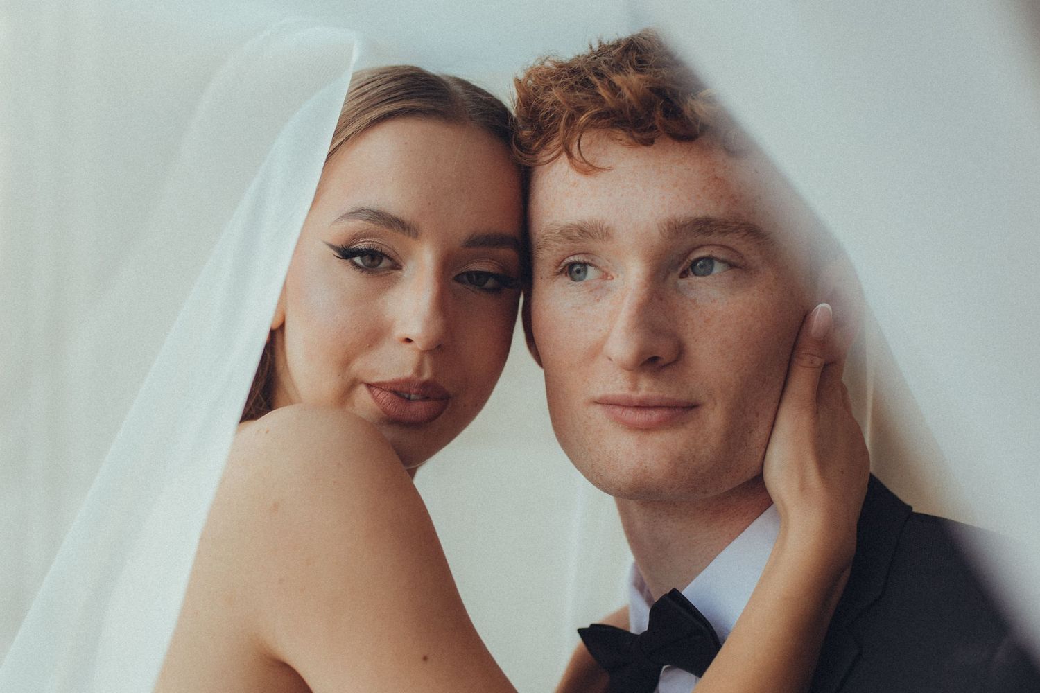 A close-up portrait of a romantic bride and groom under a veil on their wedding day.