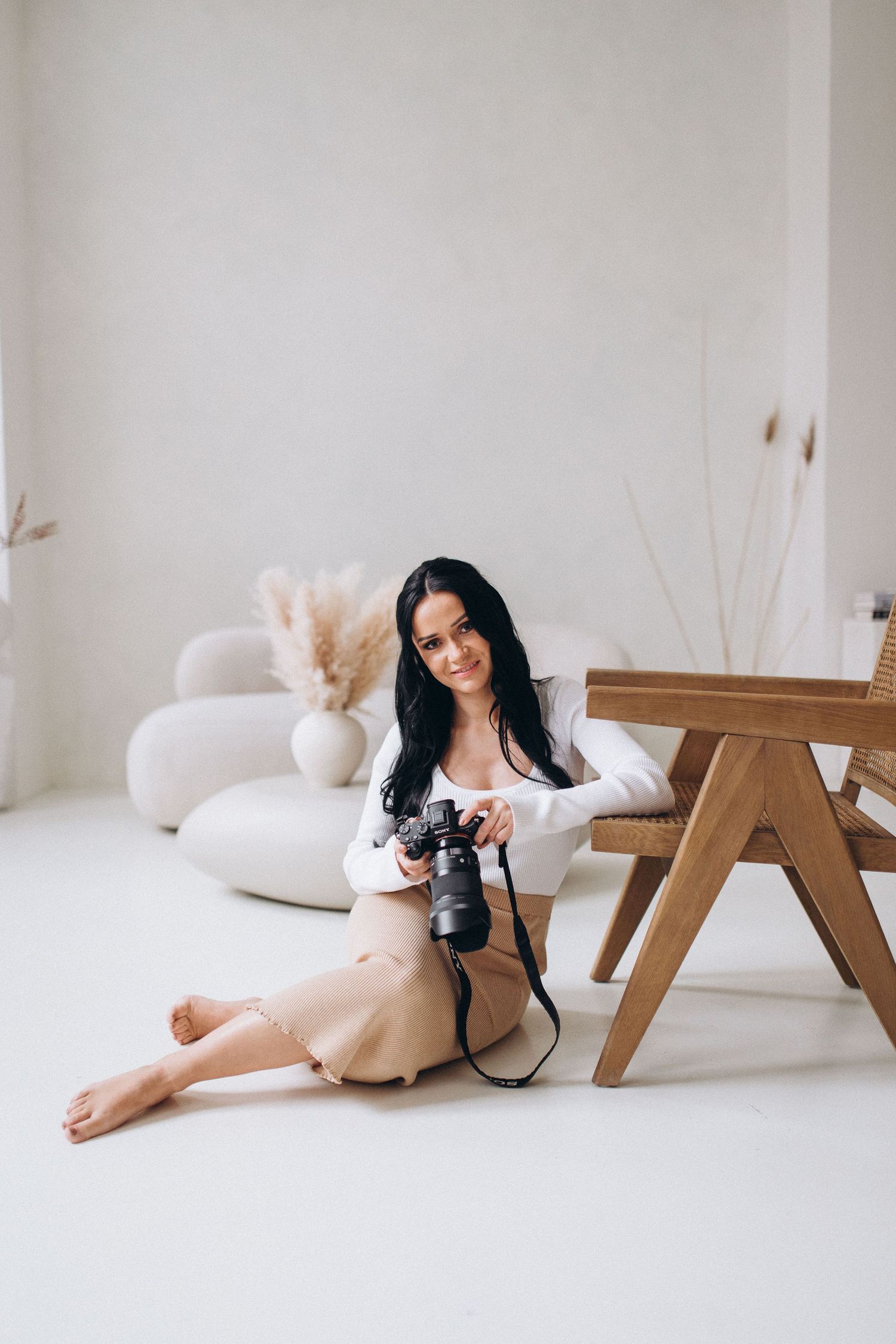 Woman in white outfit poses elegantly on floor with minimalist wooden furniture.