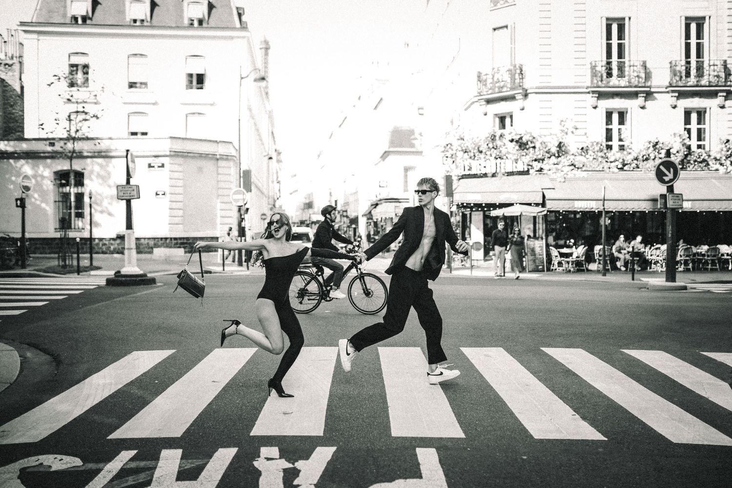 People playfully cross a zebra crossing in Paris while one person carries a bicycle in this black and white street photo.