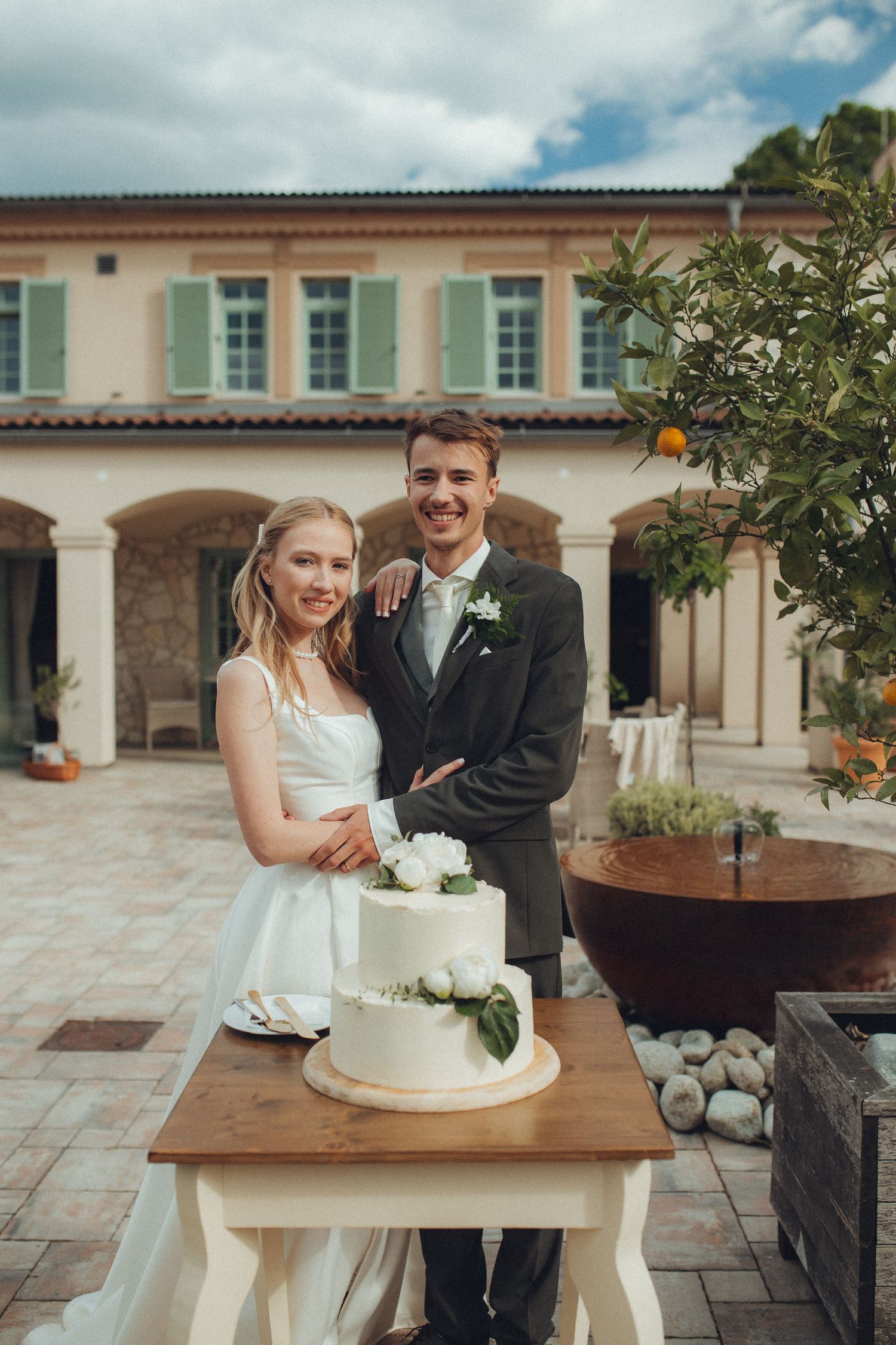 Wedding couple shares joyful moments near a rustic wooden table with white wedding cake.