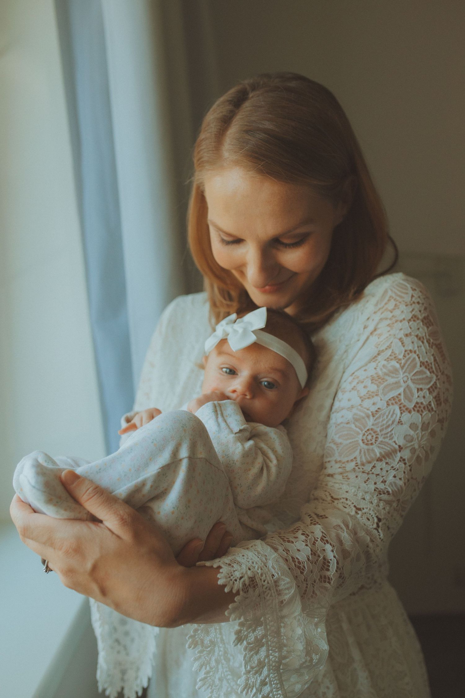 Tender moments between parent and newborn in white lace against window light.