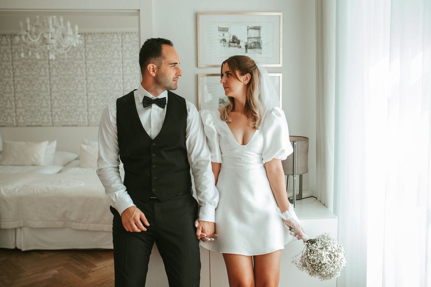 Modern wedding couple poses in bright minimalist white room with crystal chandelier.