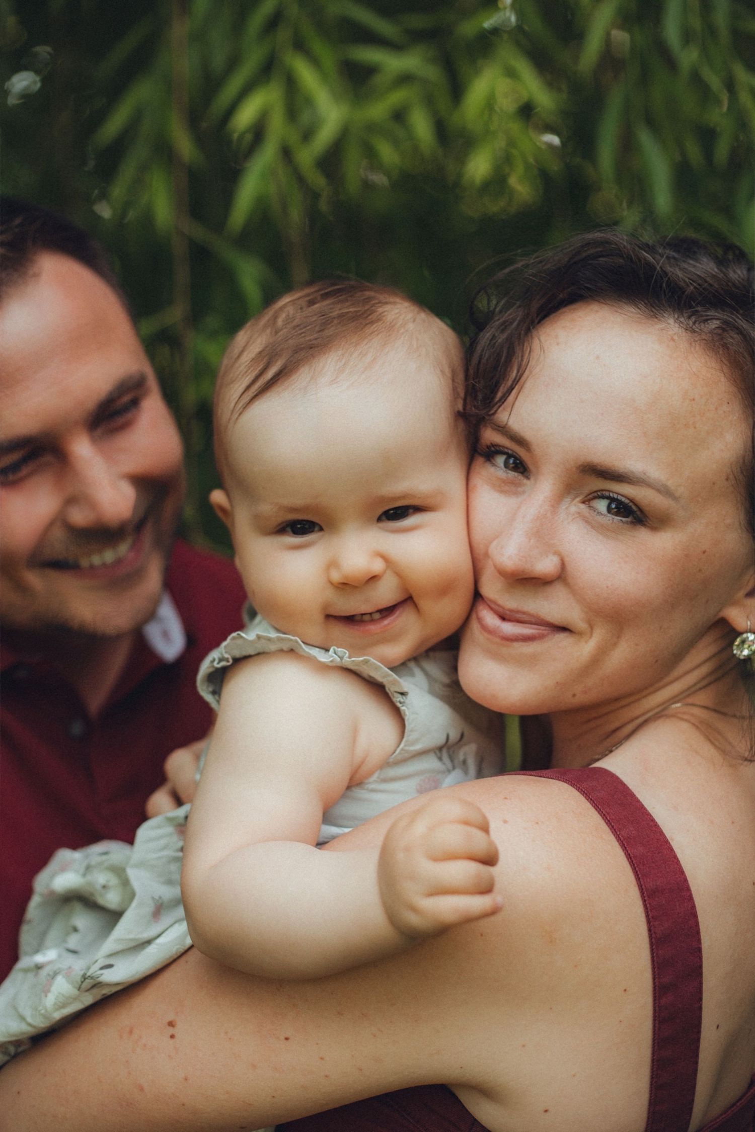 A happy family moment outdoors with a smiling baby against a leafy green background.