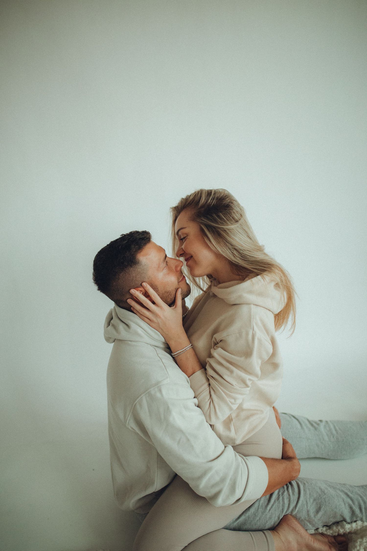 A tender embrace captured against a minimal light background in casual attire.
