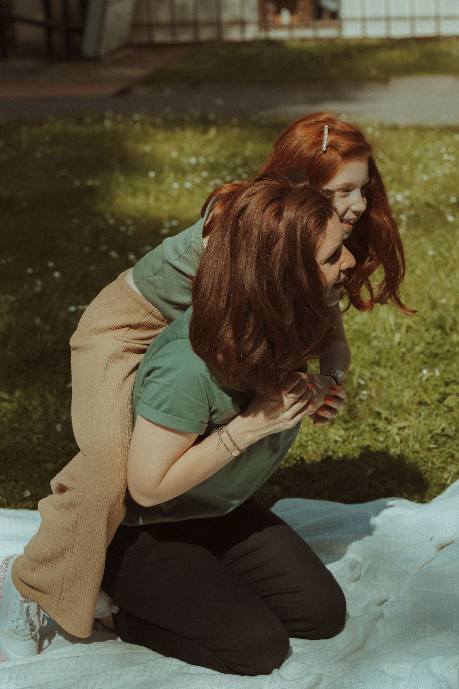 Two people sharing laughter while sitting on a picnic blanket in a grassy yard.