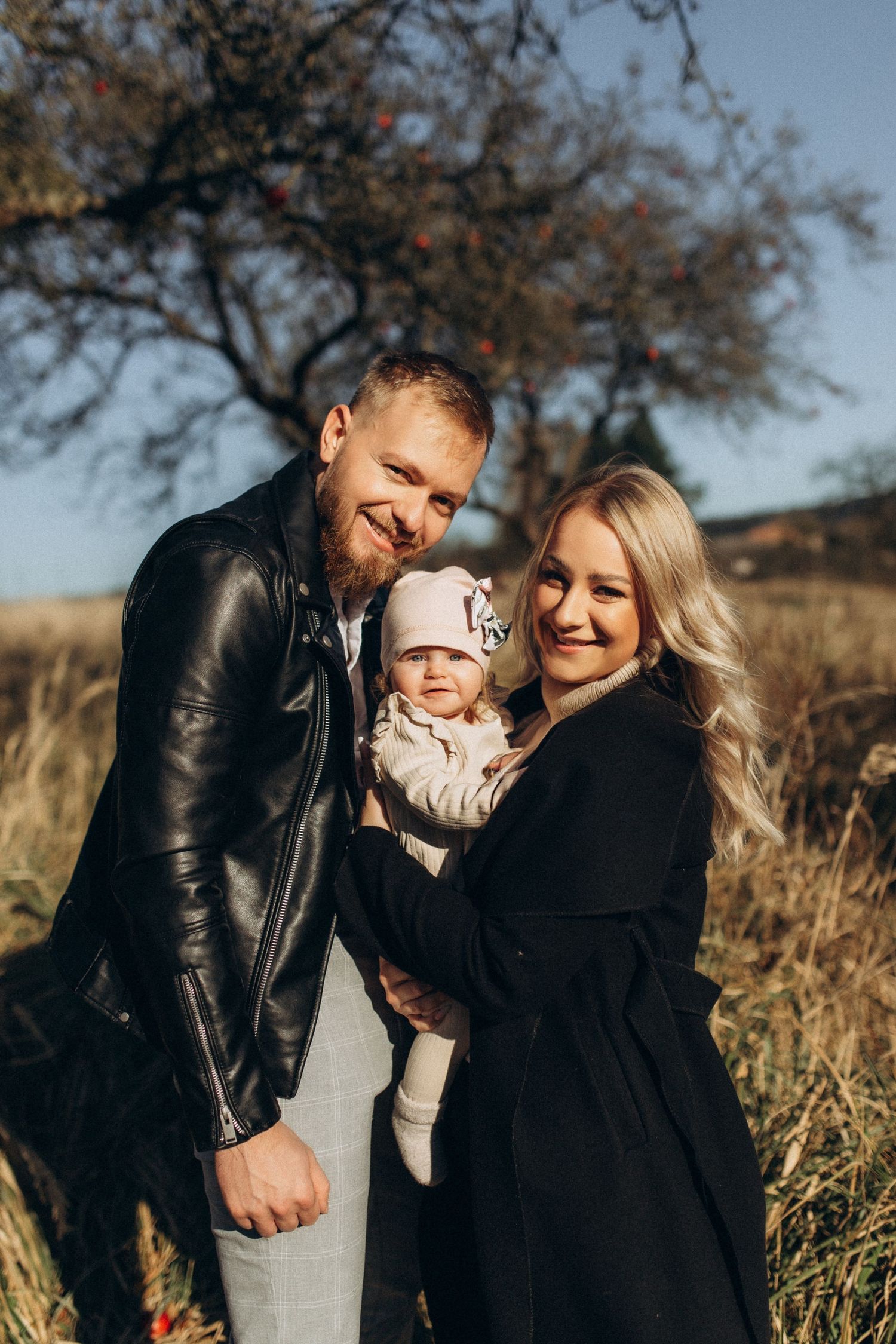 Family of three embracing and laughing together in fall field setting.