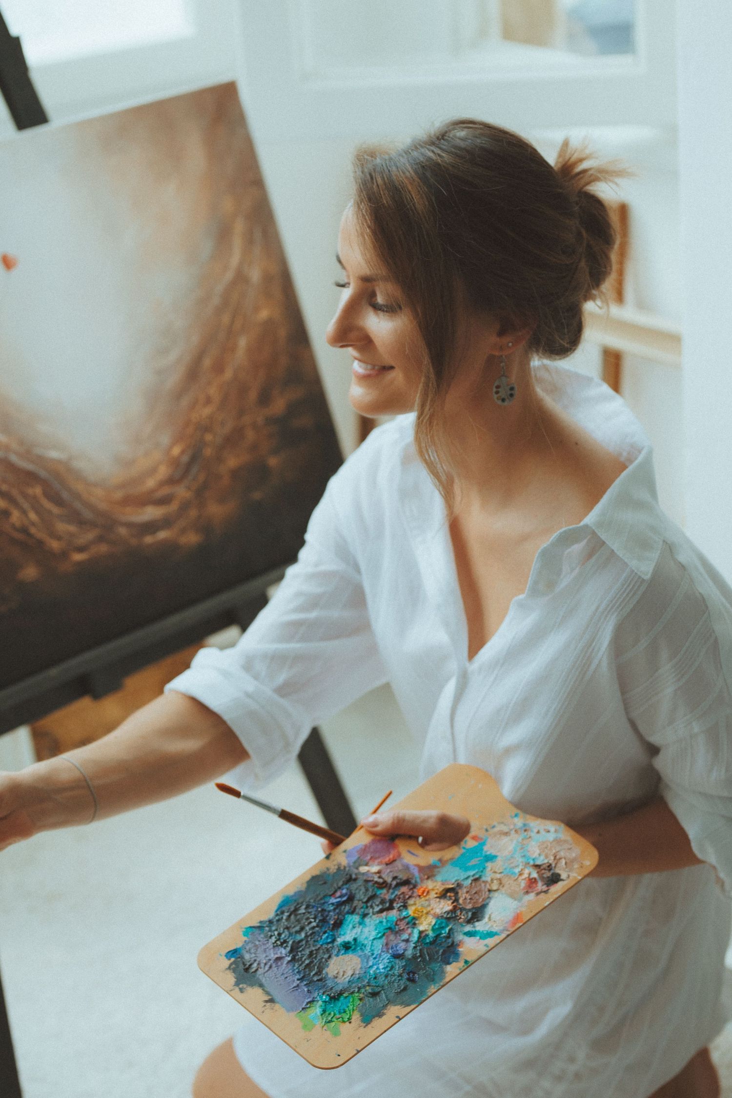 Artist in white shirt working on colorful palette in bright studio setting.