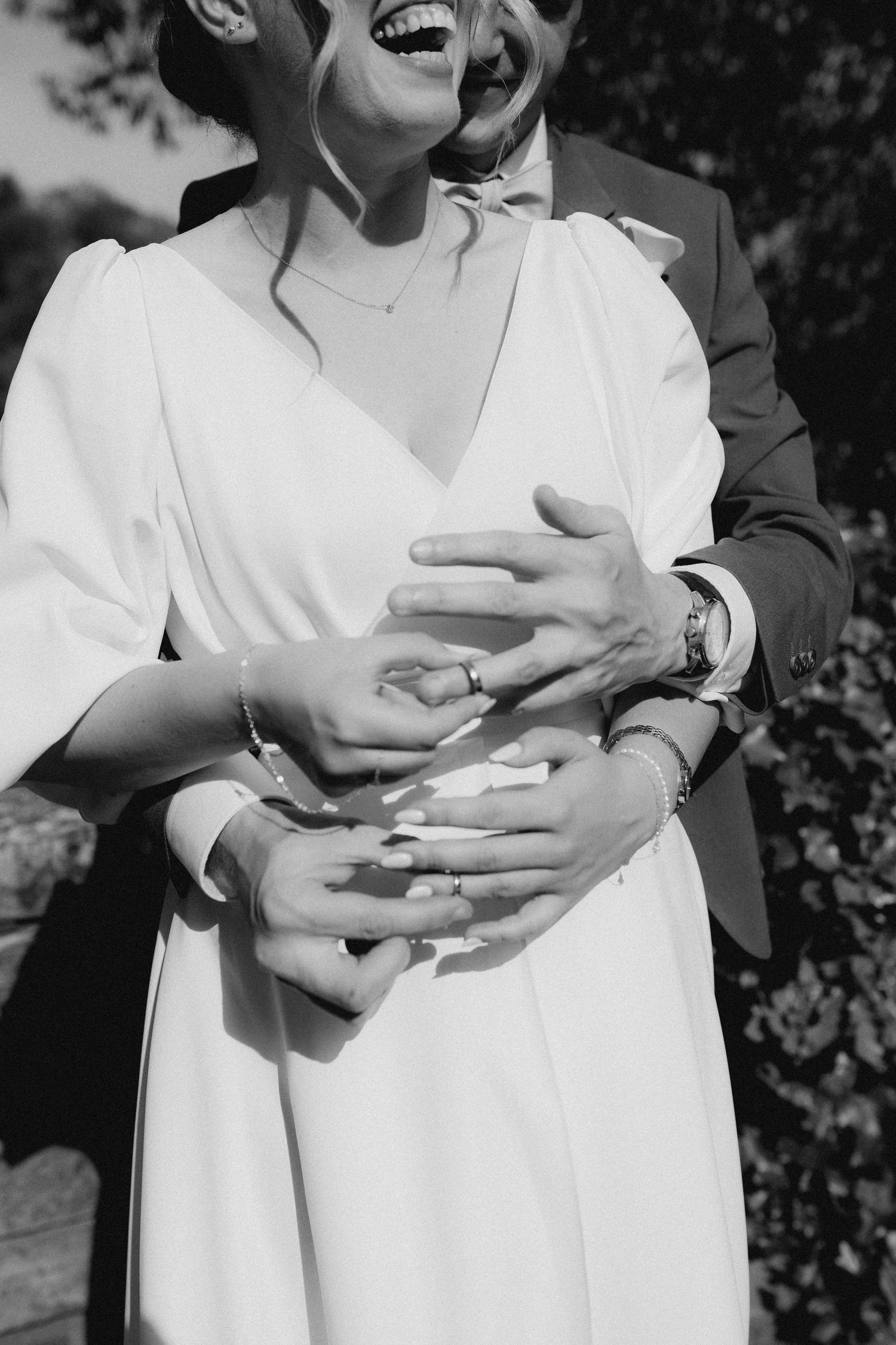Black and white photo of bride and groom embracing, showing wedding ring and bouquet petals.