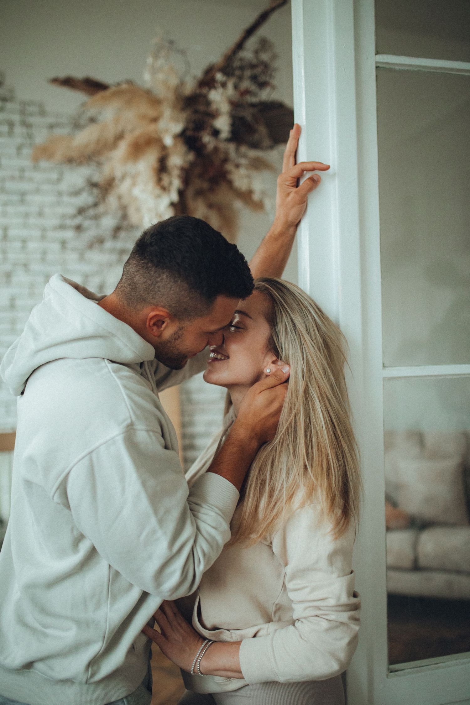 A romantic moment shared between a couple against a wall with dried floral decor.