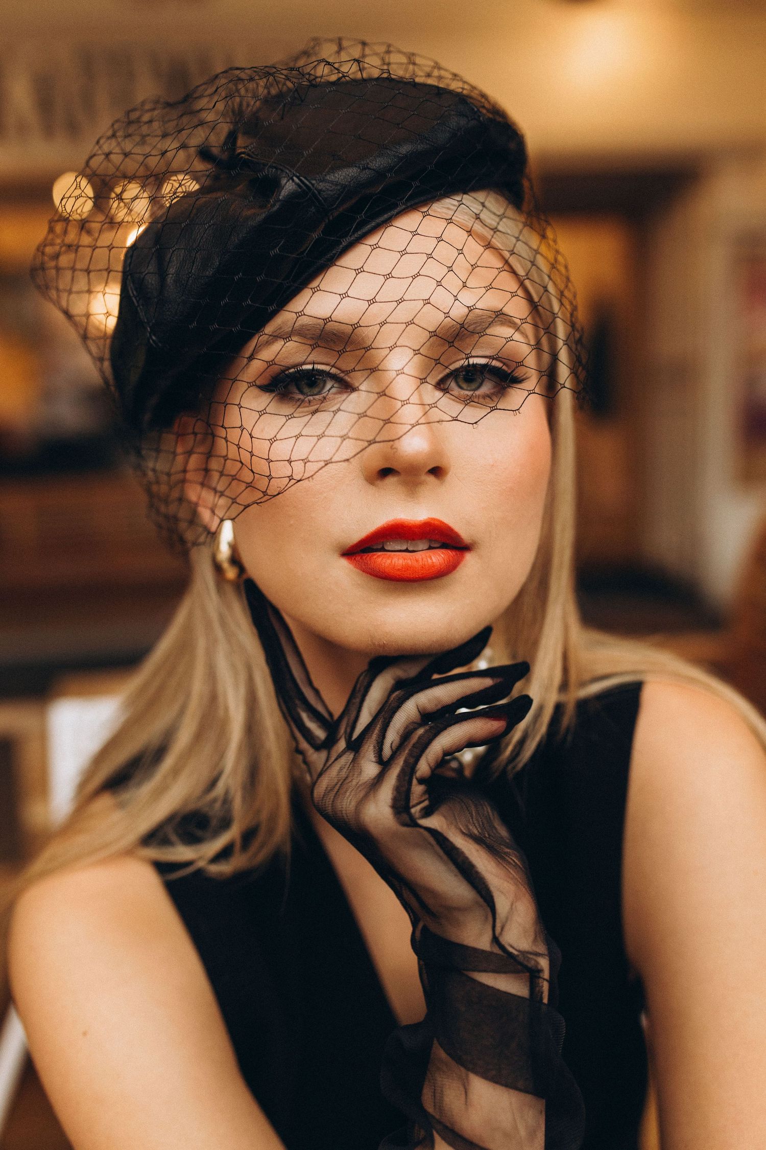 Glamorous vintage-inspired portrait with black veil and red lipstick in warm lighting.
