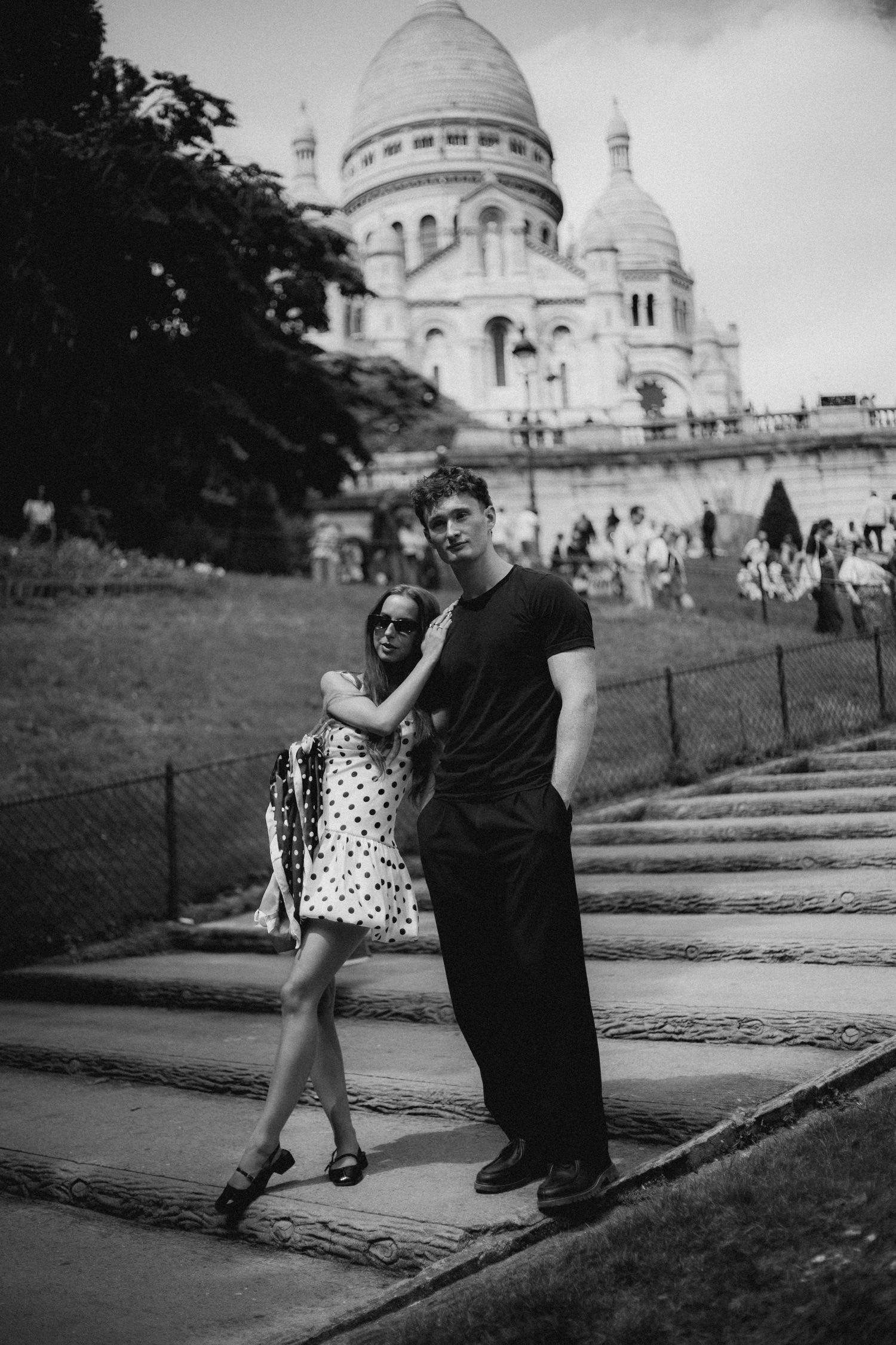 Black and white photograph showing a couple sitting in front of Sacré-Cœur Basilica in Montmartre.