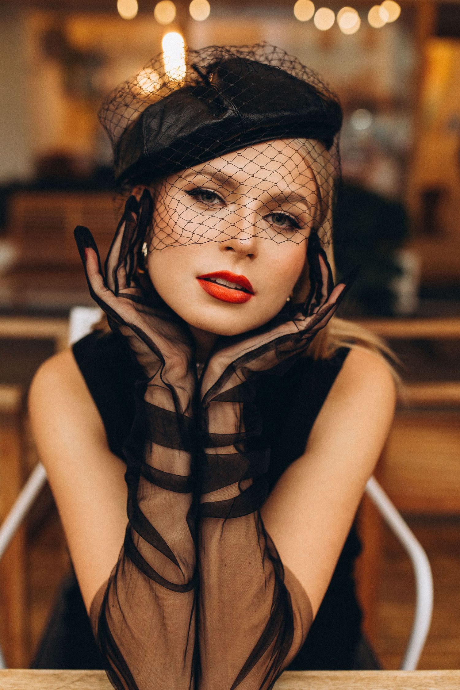 Dramatic portrait with sheer black neckwear and red lips in warm ambient cafe lighting.
