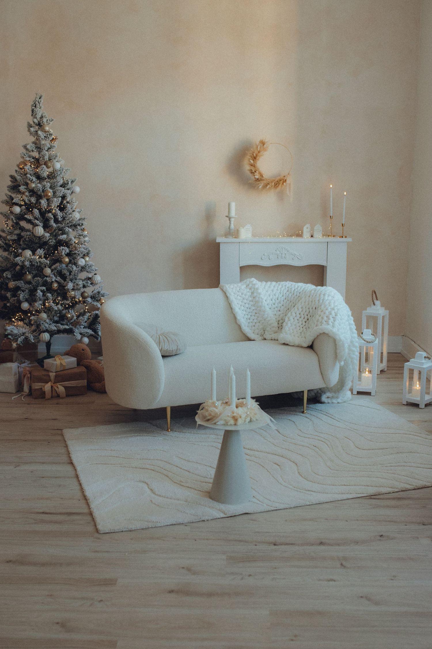 A minimalist white Christmas living room with decorated tree, vintage sofa, and candles on a light wooden floor.