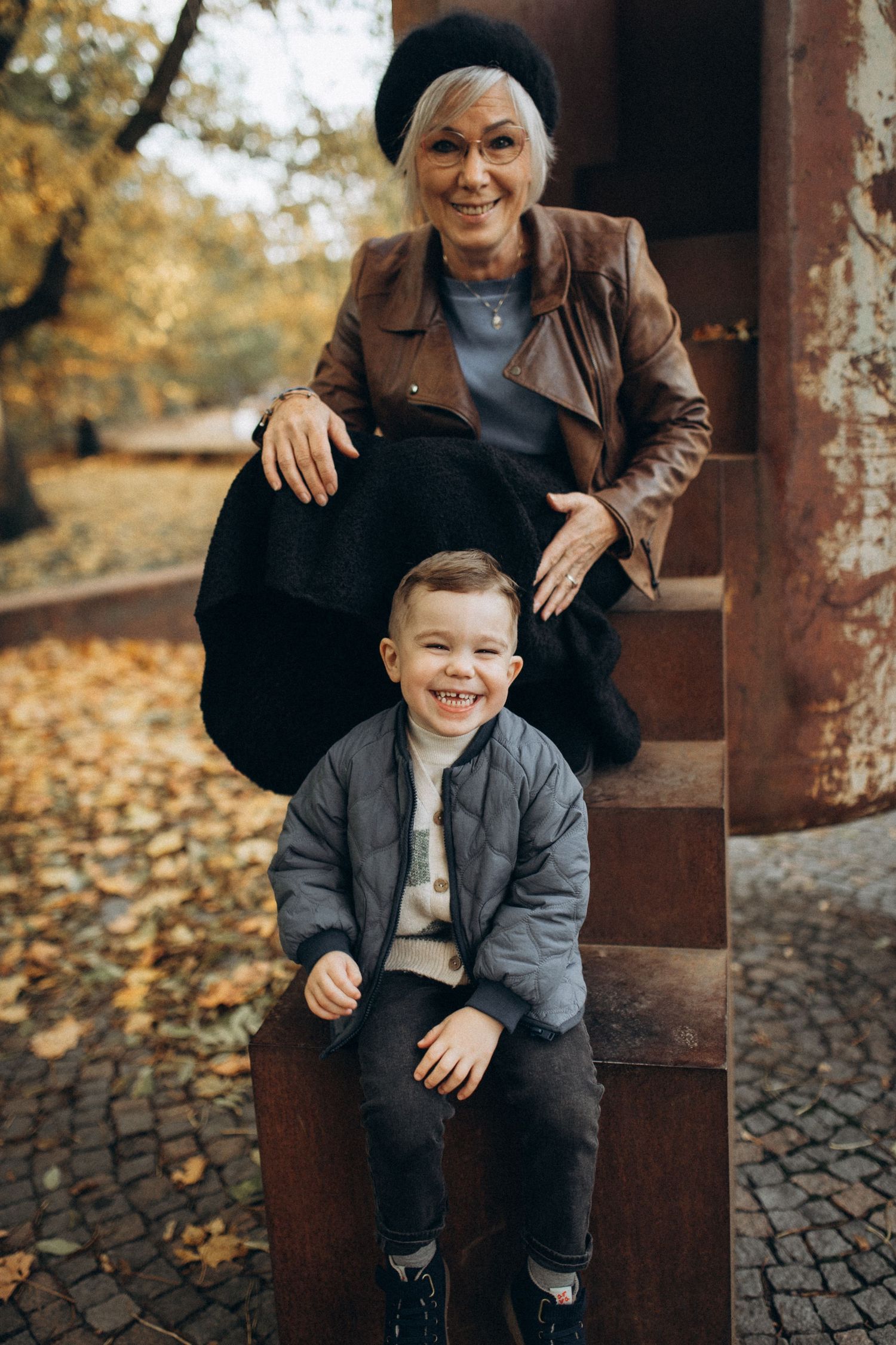 Joyful outdoor autumn portrait on stone steps with fallen leaves.
