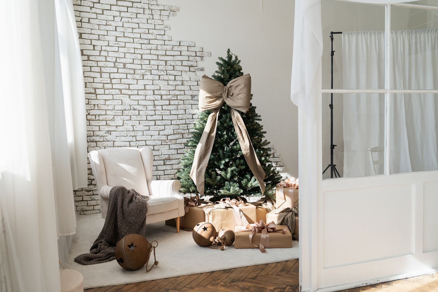 Cozy white living room with decorated Christmas tree, large bow, wrapped gifts, and brick wall backdrop.
