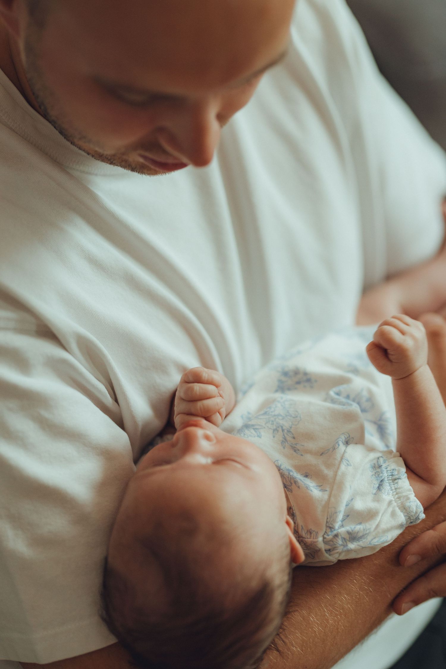 Parent cradling sleeping newborn baby in white shirt.