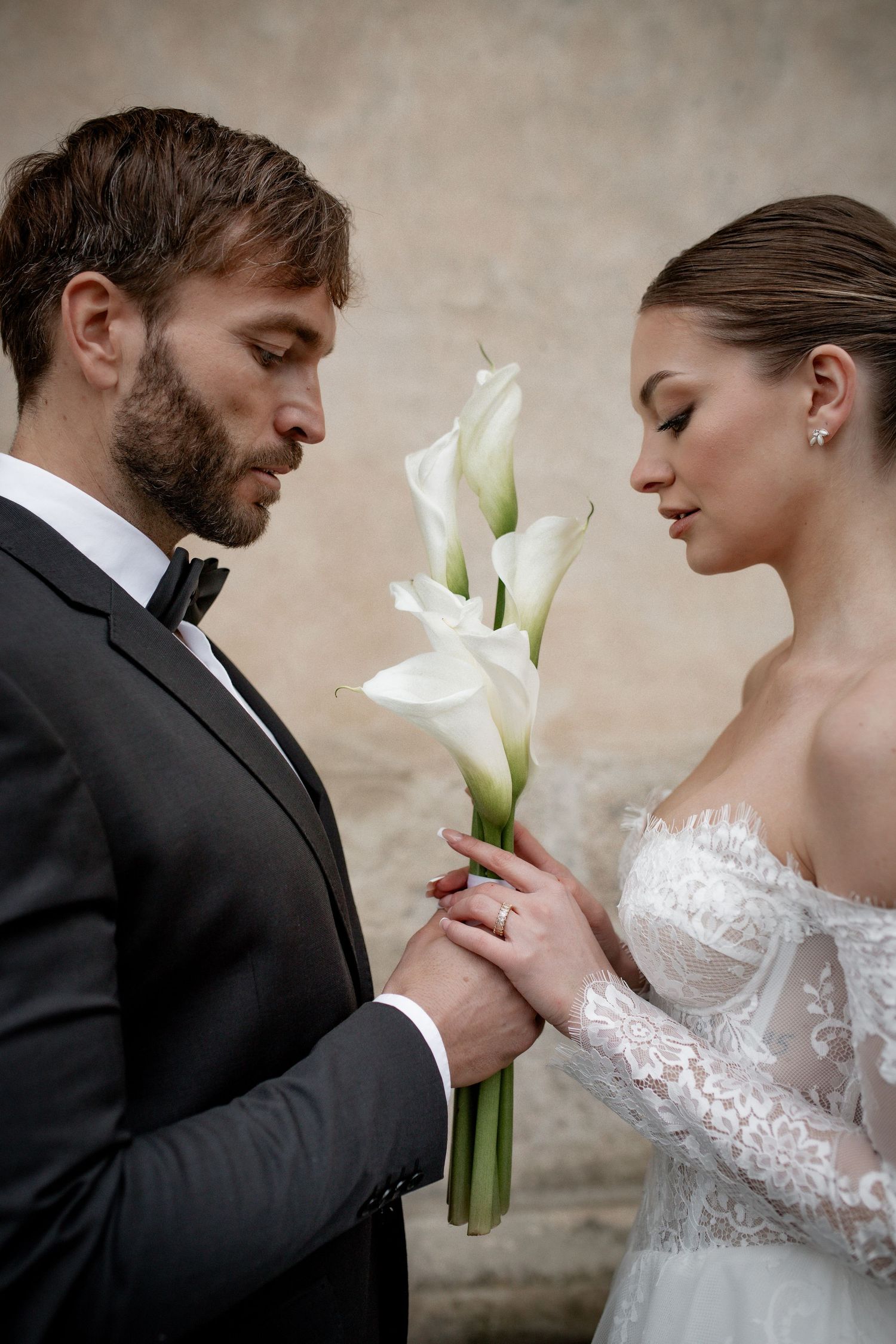 Bride and groom holding white calla lily bouquet together in elegant wedding attire, sharing an intimate moment.