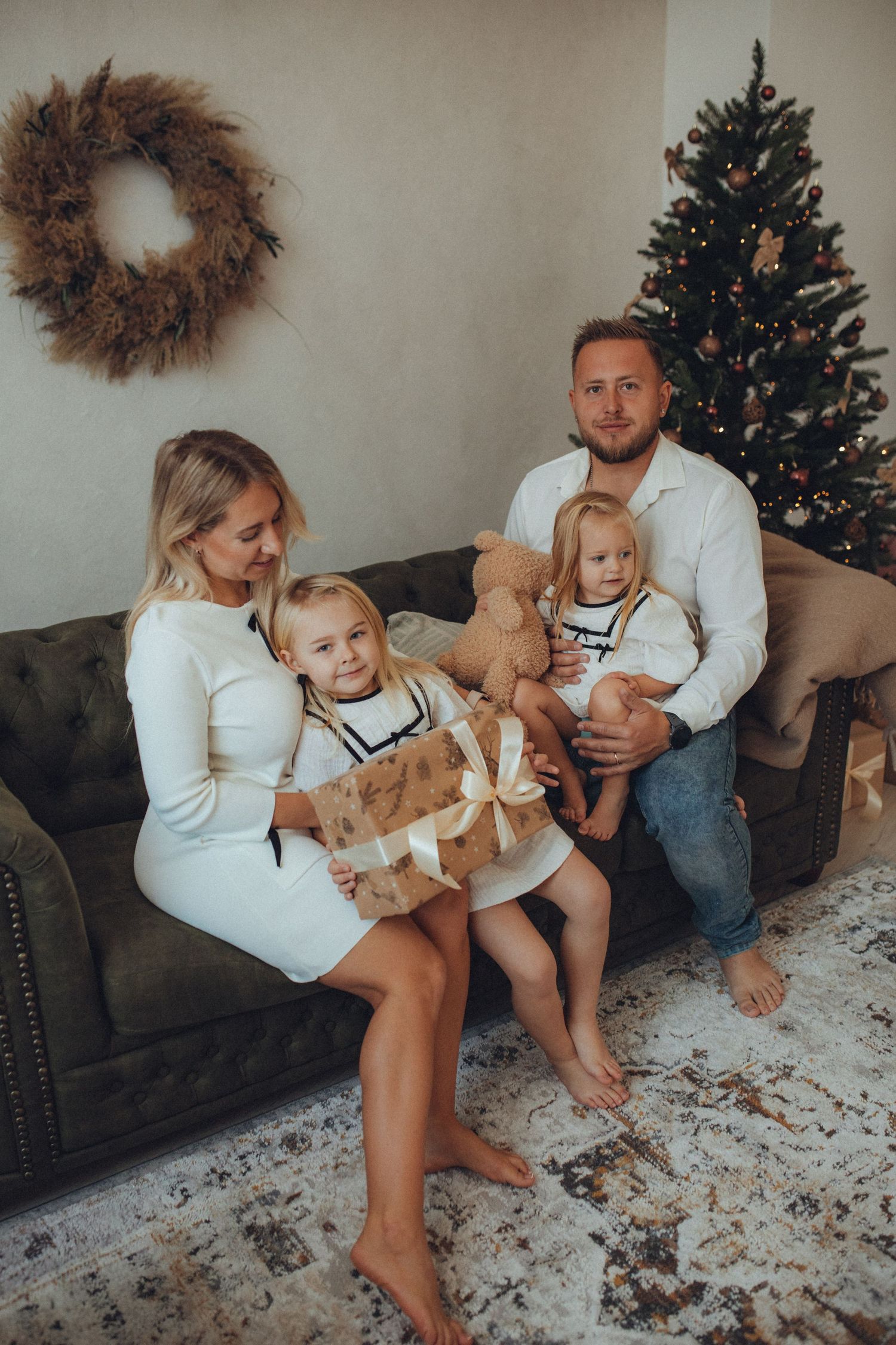 A family sits together on a grey couch with their golden retriever puppy during Christmas time.