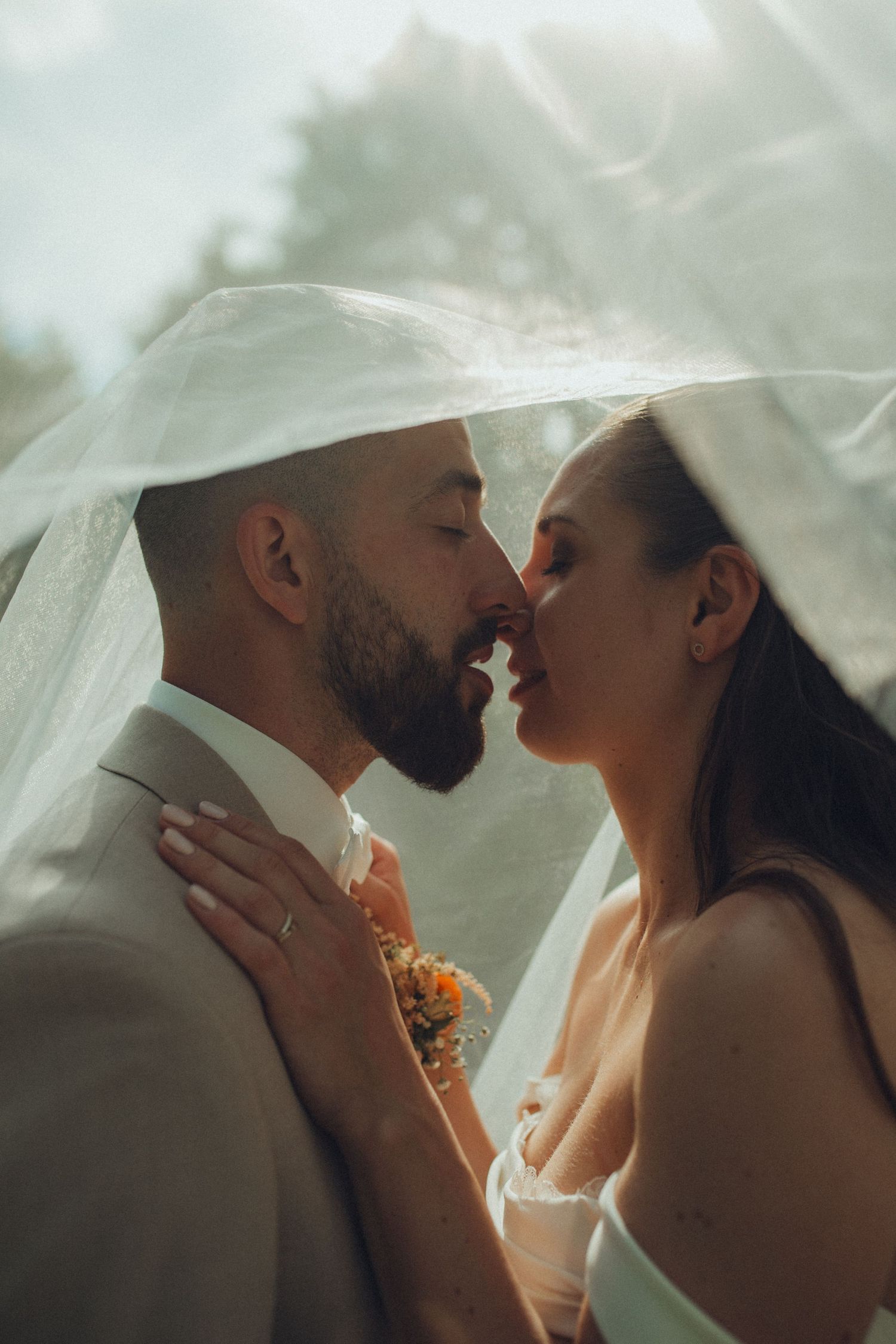 A tender moment between newlyweds as they share an intimate kiss under a flowing white veil.