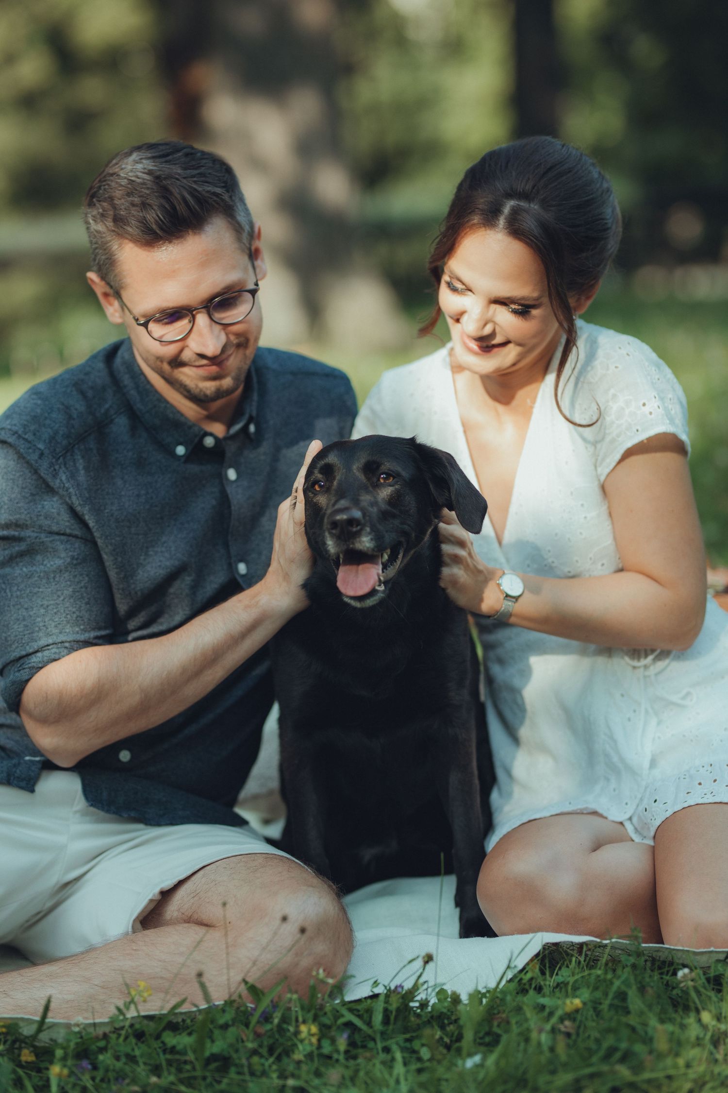 Couple enjoying outdoor picnic with happy black dog sitting between them.