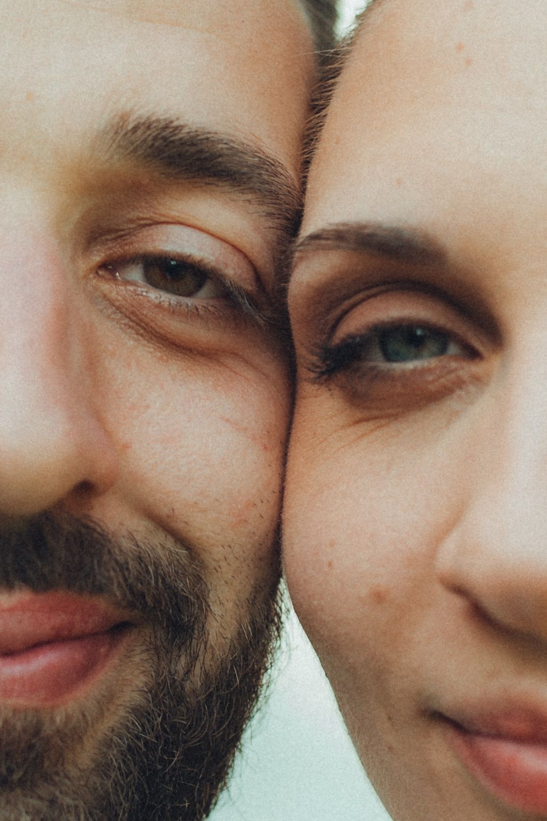 Close-up portrait showing two smiling faces side by side in romantic gentle lighting.
