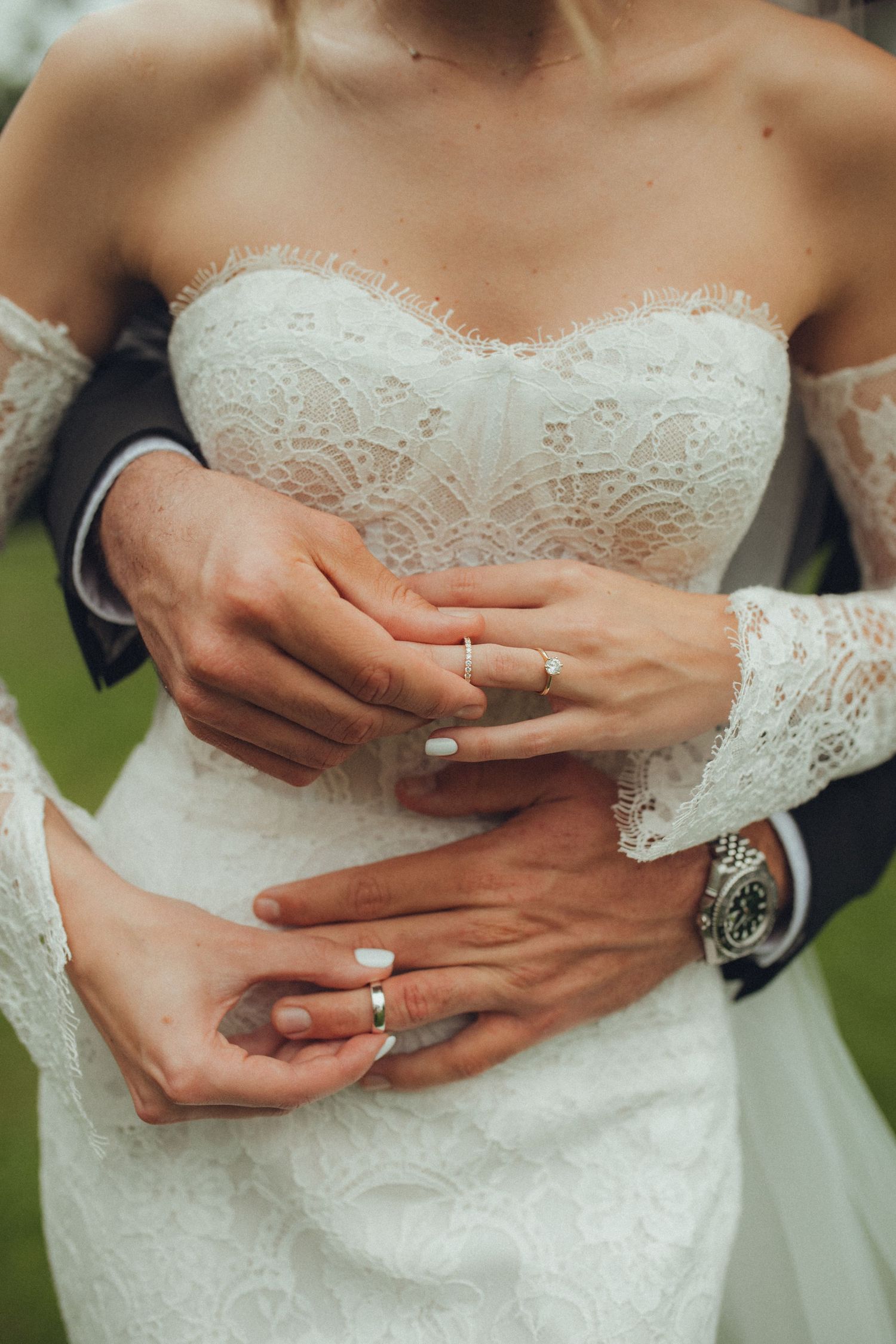Close-up of hands showing wedding rings against white lace wedding dress.