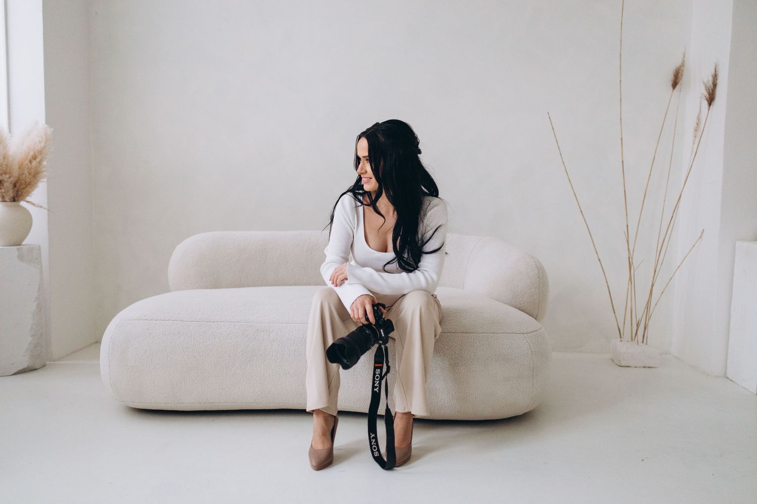 Photographer sitting on white couch examining camera equipment.
