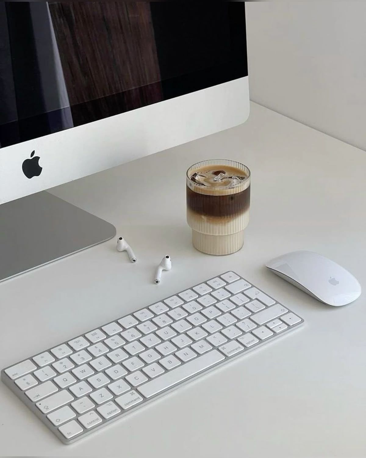Minimalist white desk setup with Apple iMac, keyboard, mouse and layered coffee drink.