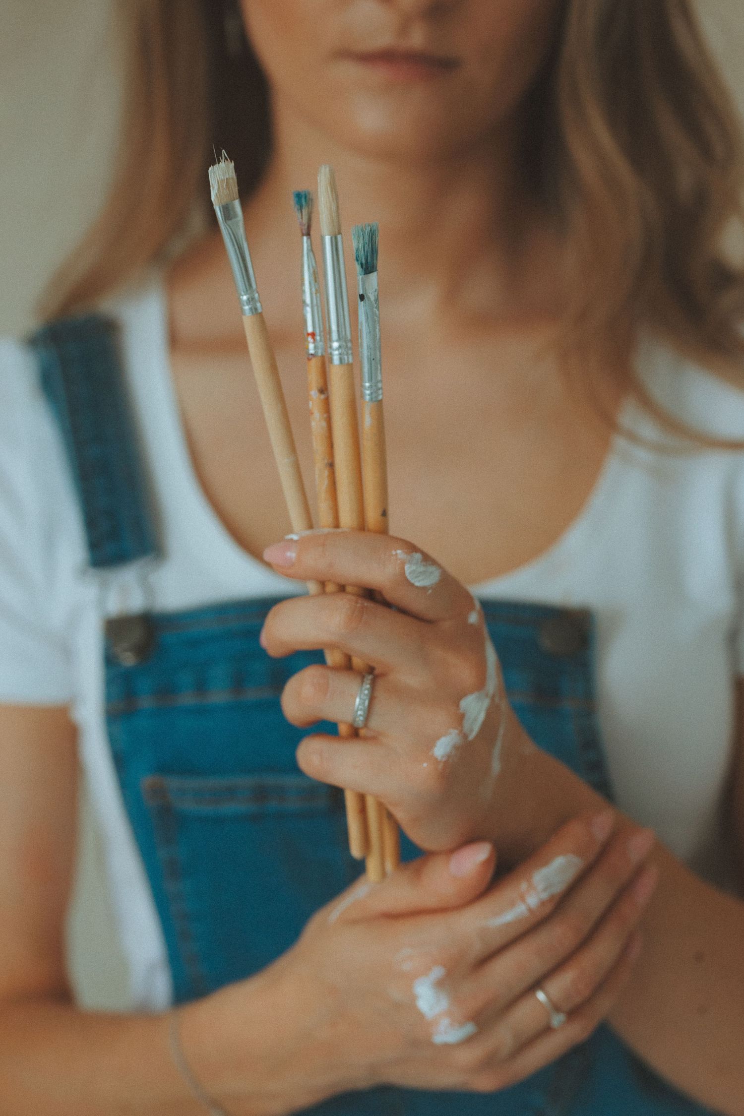 Hands holding paint brushes with turquoise tips against light background.