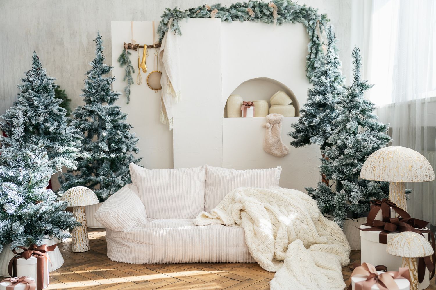 Cozy white Christmas living room with flocked pine trees, gift boxes, and festive garland decor.
