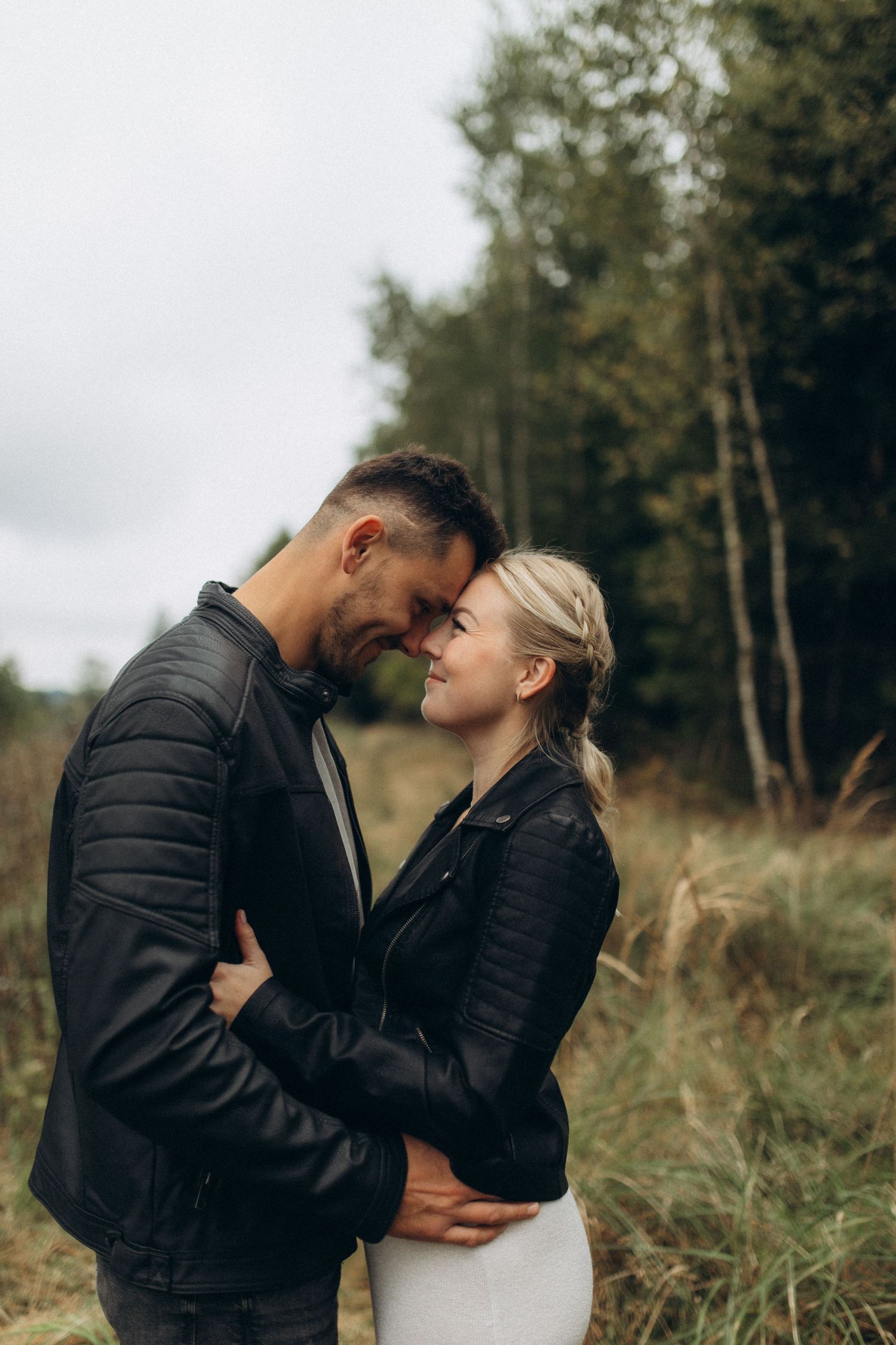 A couple shares an intimate moment while standing in tall grass with trees in the background.