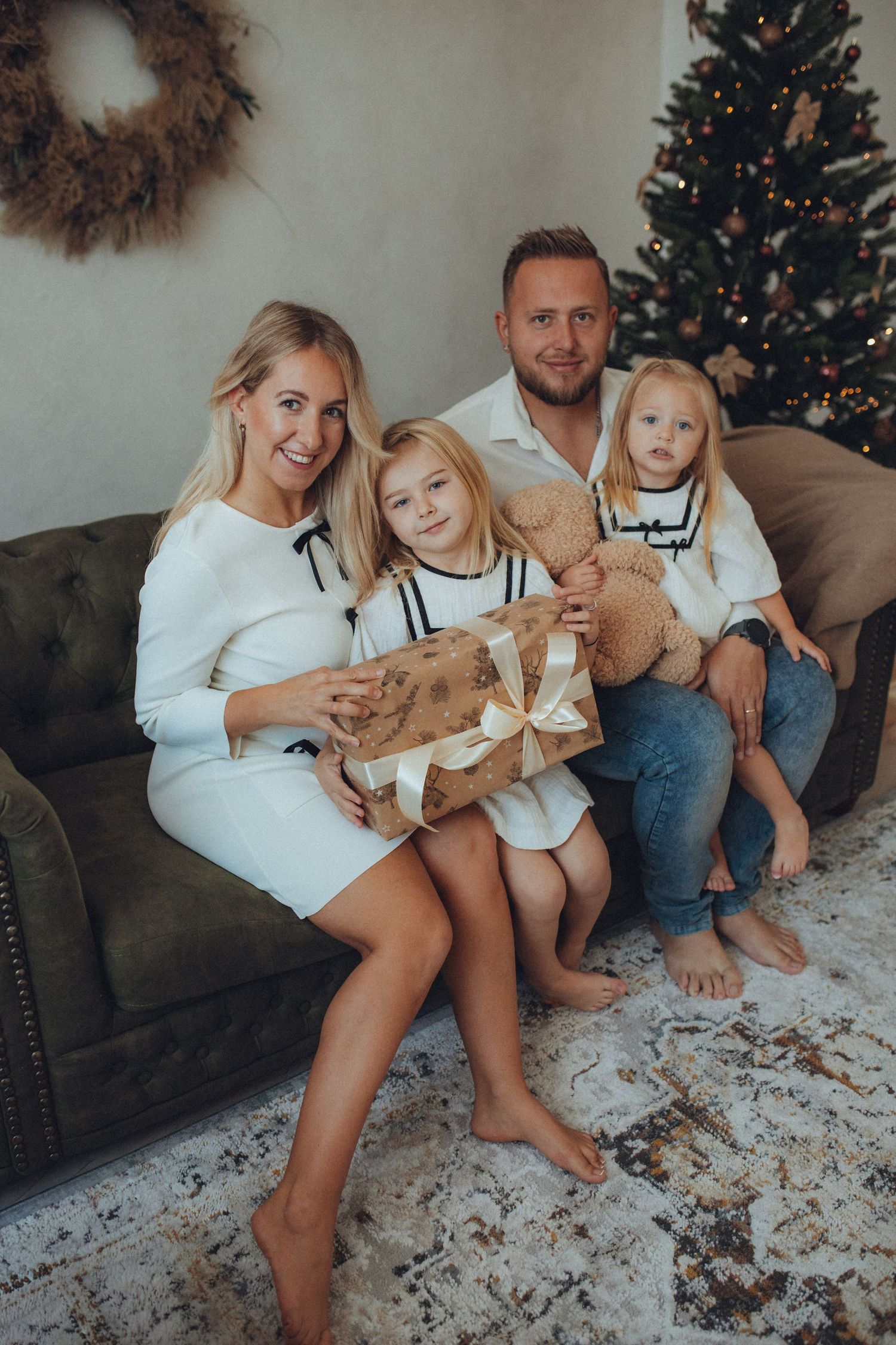 A family sits together on a gray couch during the holidays with a decorated Christmas tree in the background.