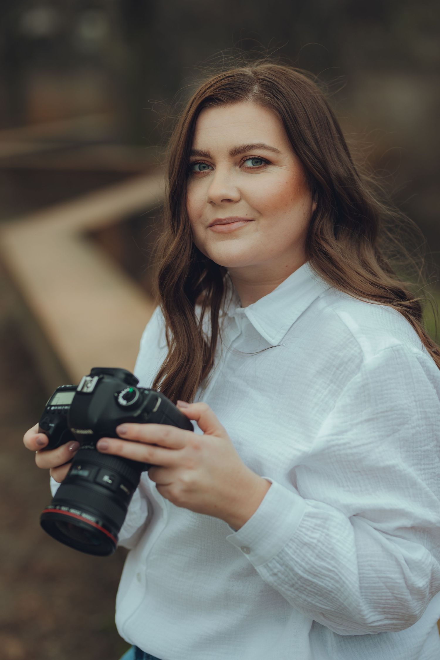 Person in white button-down shirt holding professional camera in outdoor setting.
